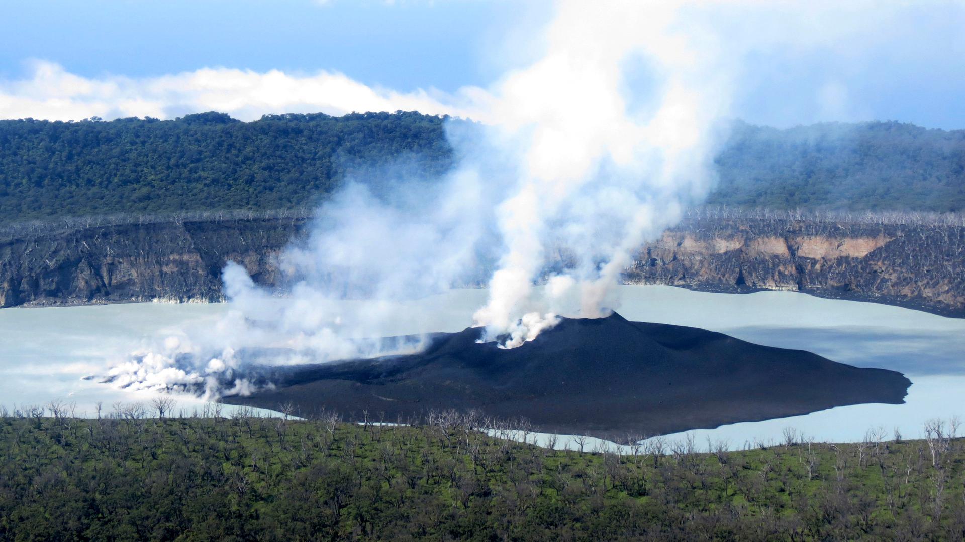 A dark volcano with smoke rising out of it surrounded by a body of water.