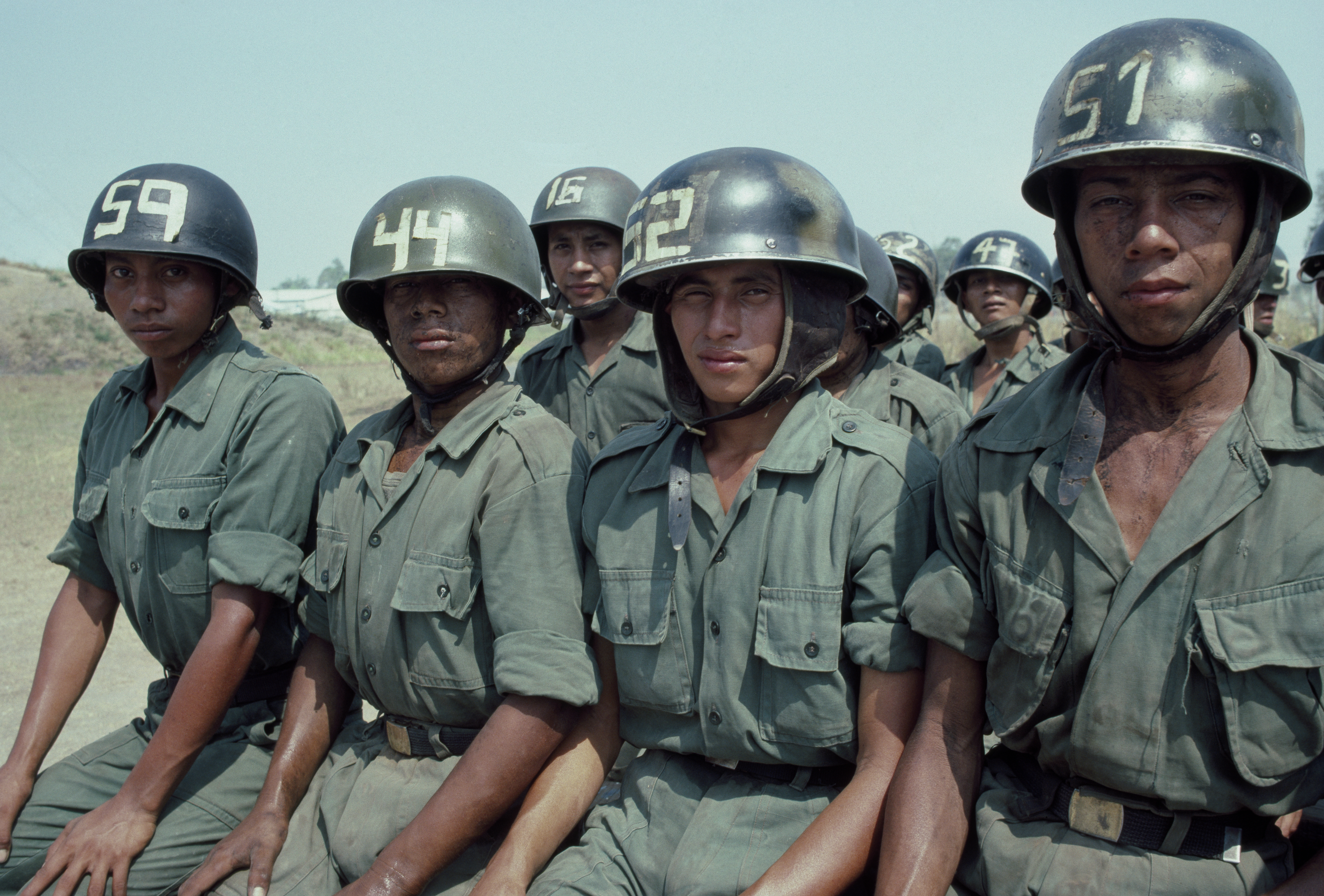 Four women dressed in Army green and helmets sit side by side and make eye contact with the camera.