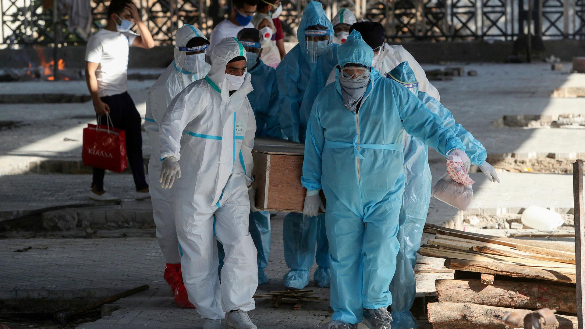Several people are show wearing protective medical clothing and carrying a wooden casket.