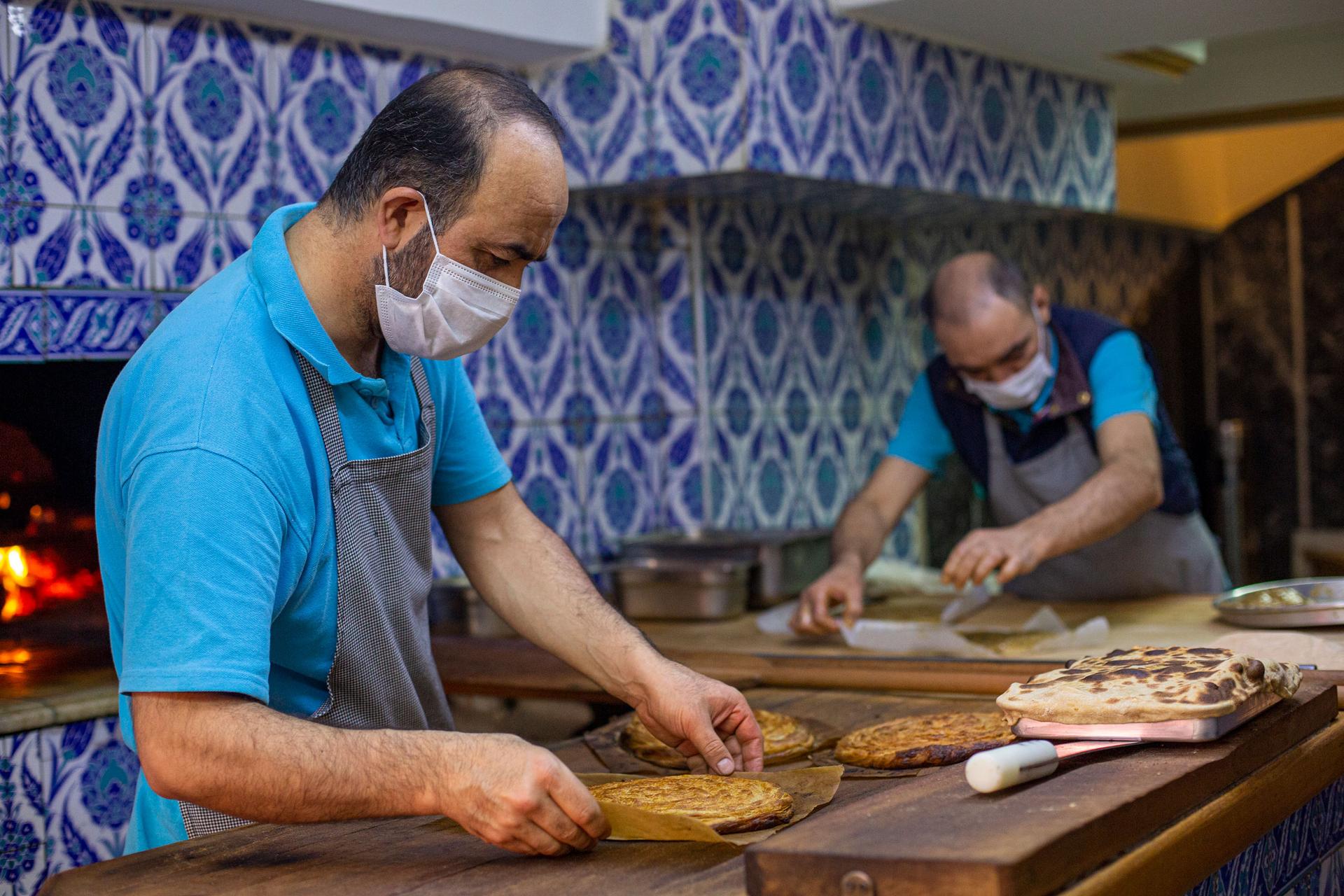 A man is shown wearing a blue shirt and gray aprin while handling a flat bread-like dish.