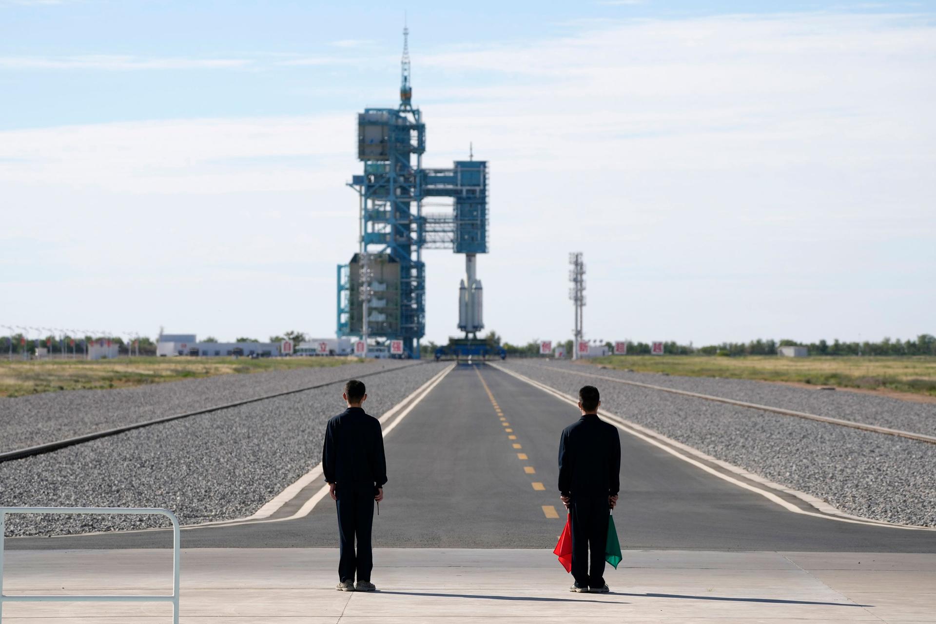 Two people are shown at the end of a long tarmac with the Chinese spaceship set for launch in the distance.