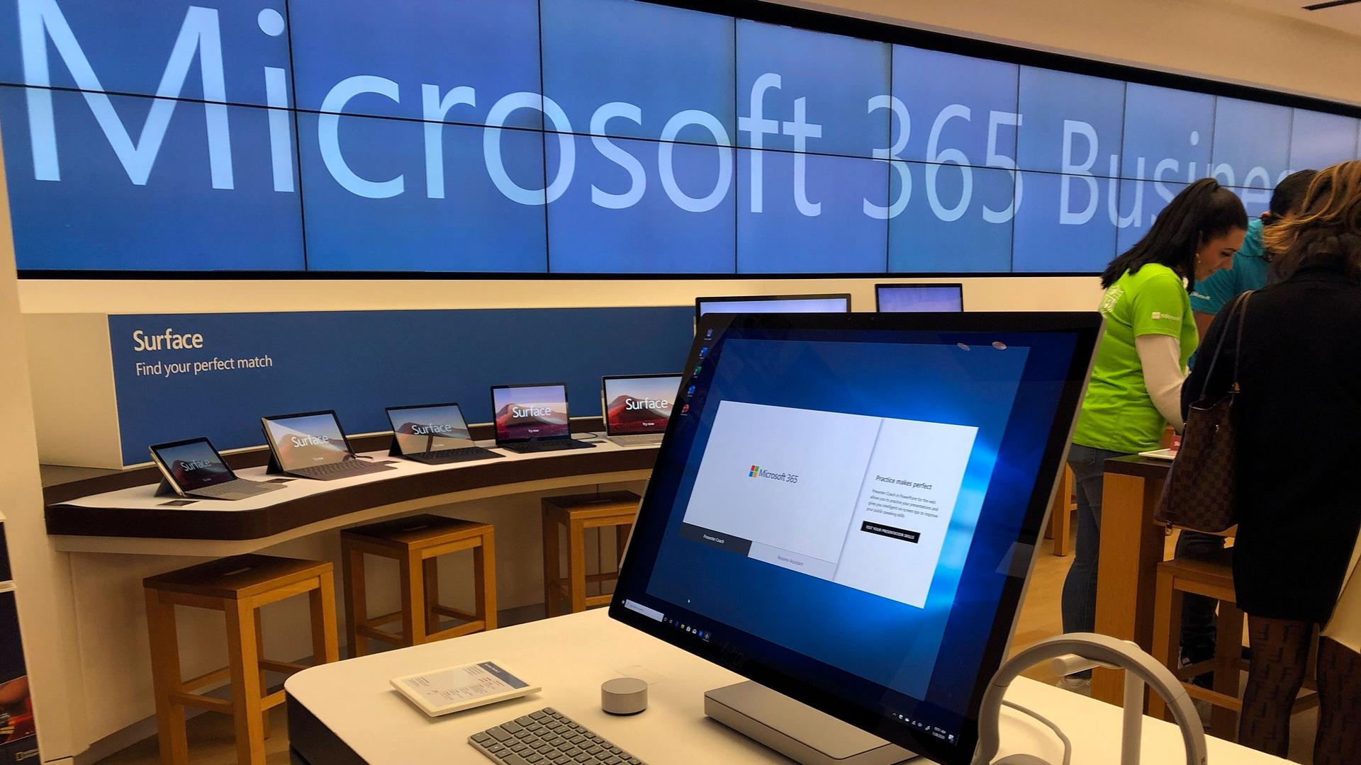 A computer monitor is shown in the nearground with a row of tablet computers in the distance under a Microsoft banner.