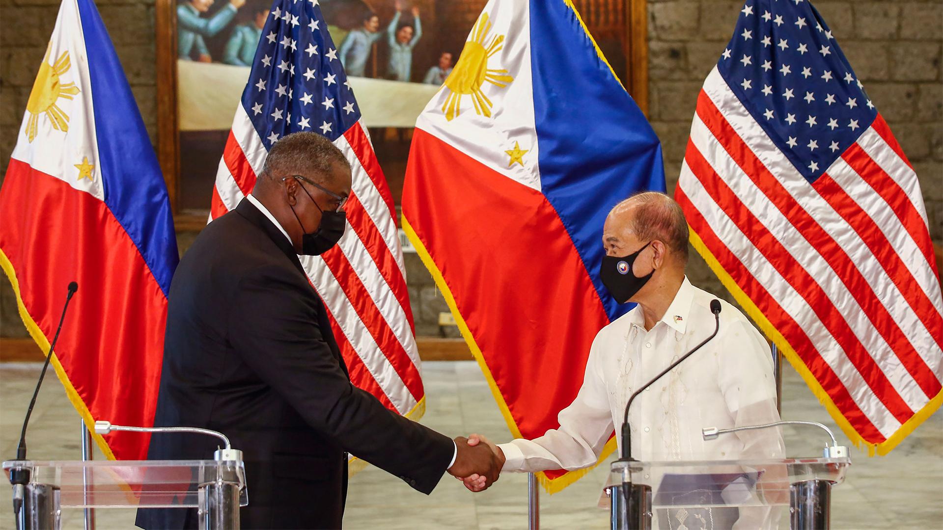 United States Defense Secretary Lloyd Austin and Philippines Defense Secretary Delfin Lorenzana shake hands after a bilateral meeting with their counties' flags behind them