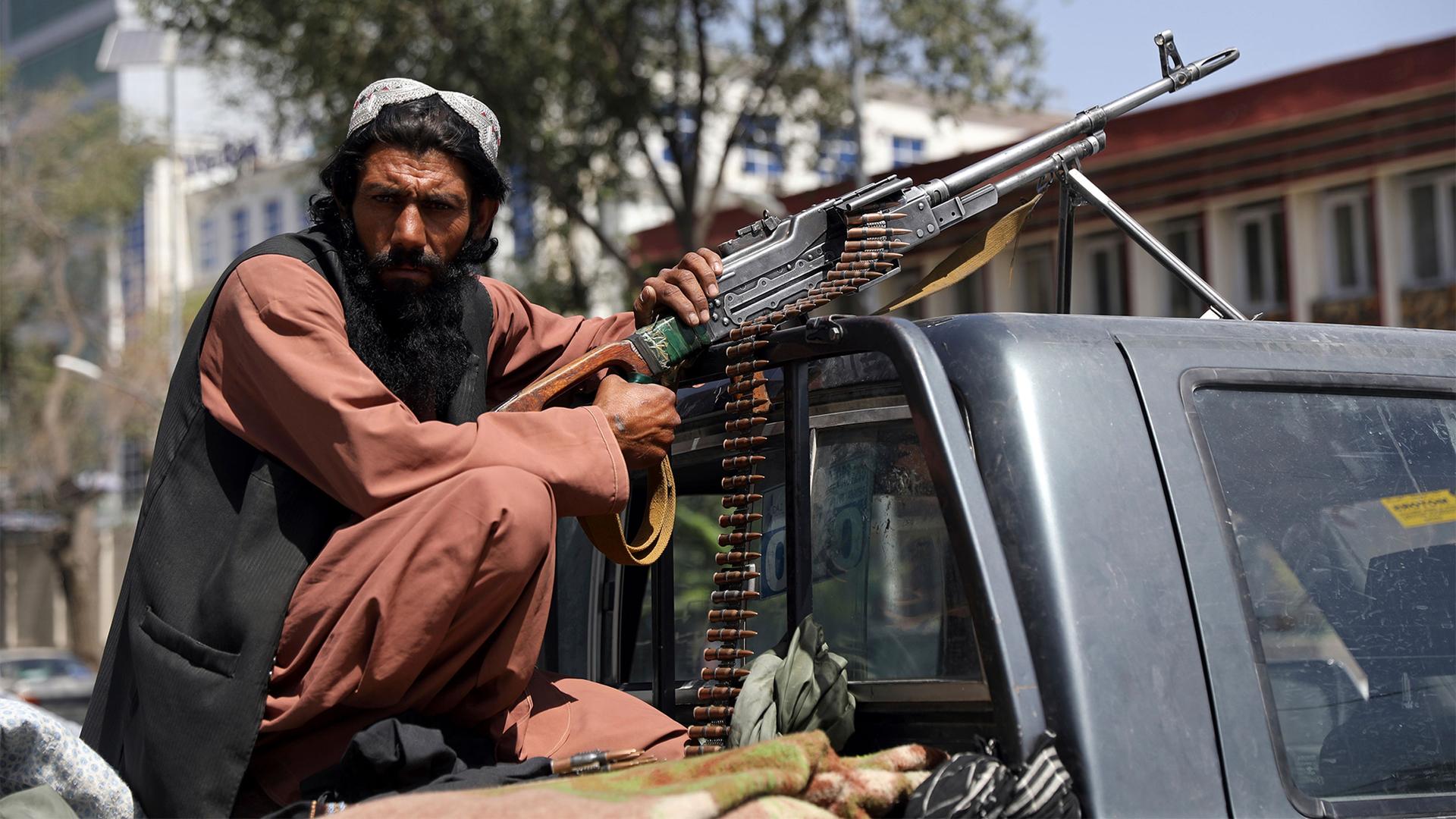 A Taliban fighter sits on the back of a vehicle with a machine gun in front of the main gate leading to the Afghan presidential palace