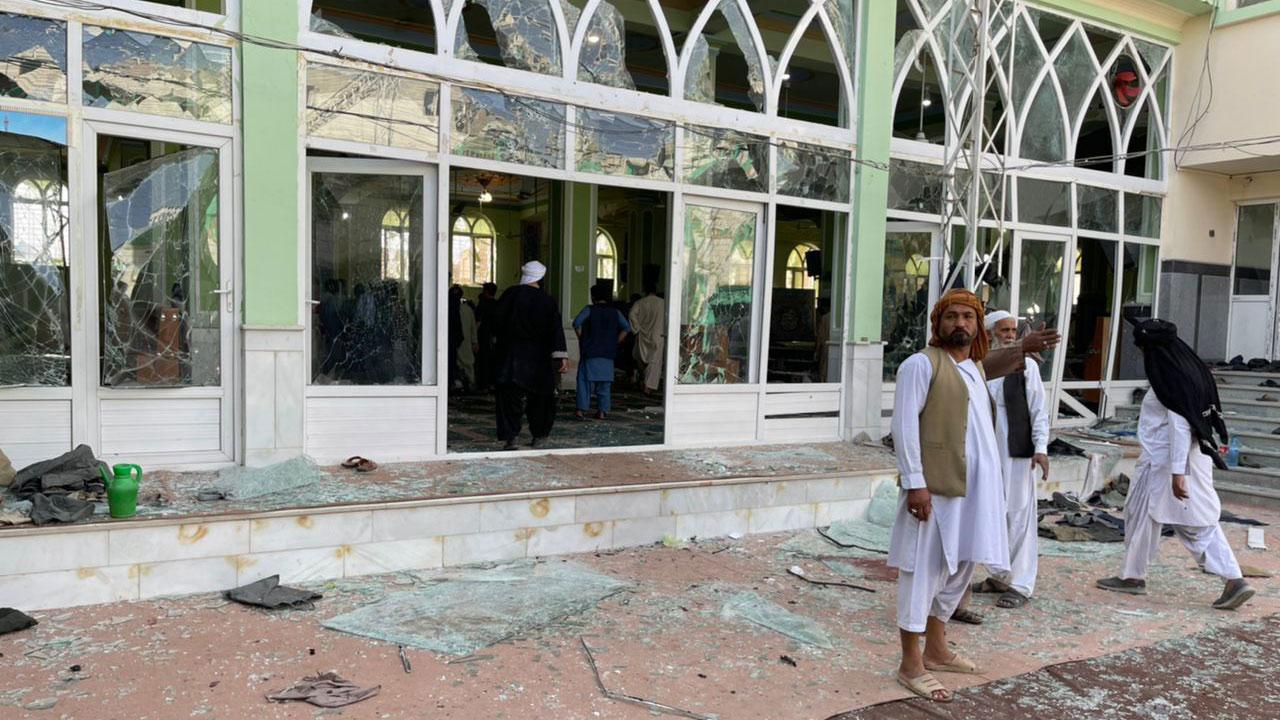 Three men are show wearing white traditional clothing and standing amidst broken glass from a mosque in the background.
