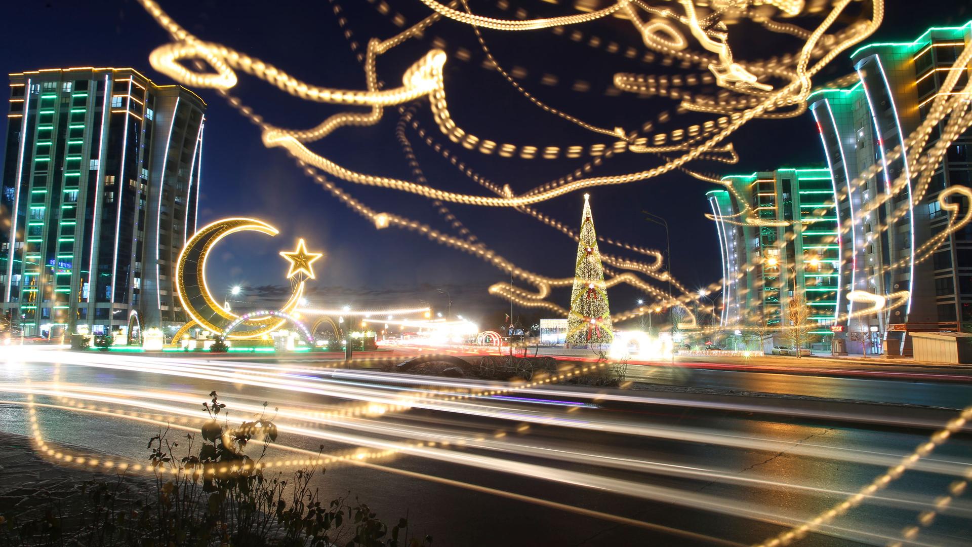 A crescent and apartments buildings decorated for New Year celebrations are seen through a window reflecting a holiday light at the central square in Argun, the capital of Chechen republic, Russia, Thursday, Dec. 23, 2021. 