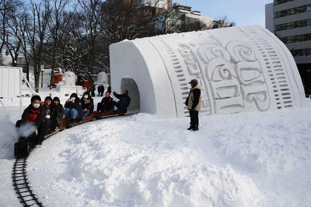 Riders on a tiny train go into a giant snow sculpture of a cup of noodles