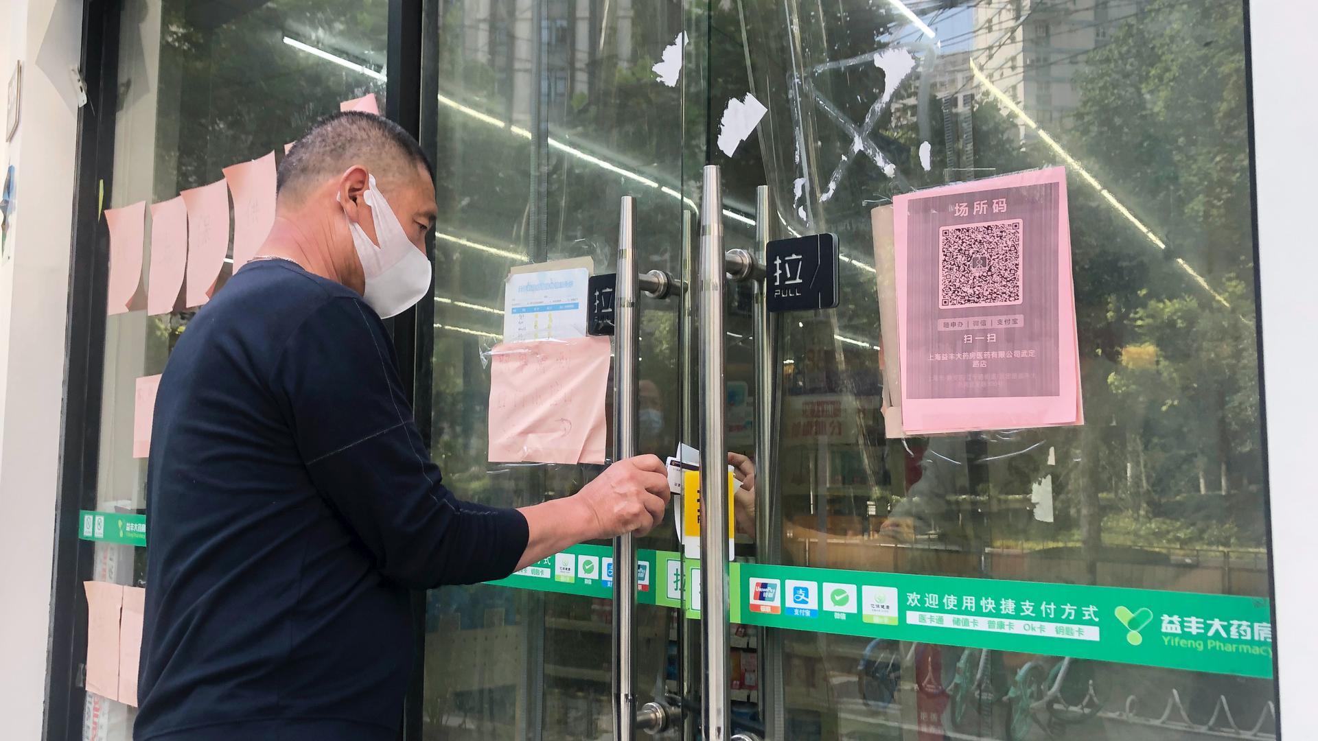 A man tries to receive medicine he bought at a pharmacy through its closed glass doors in Shanghai, China, May 22, 2022.