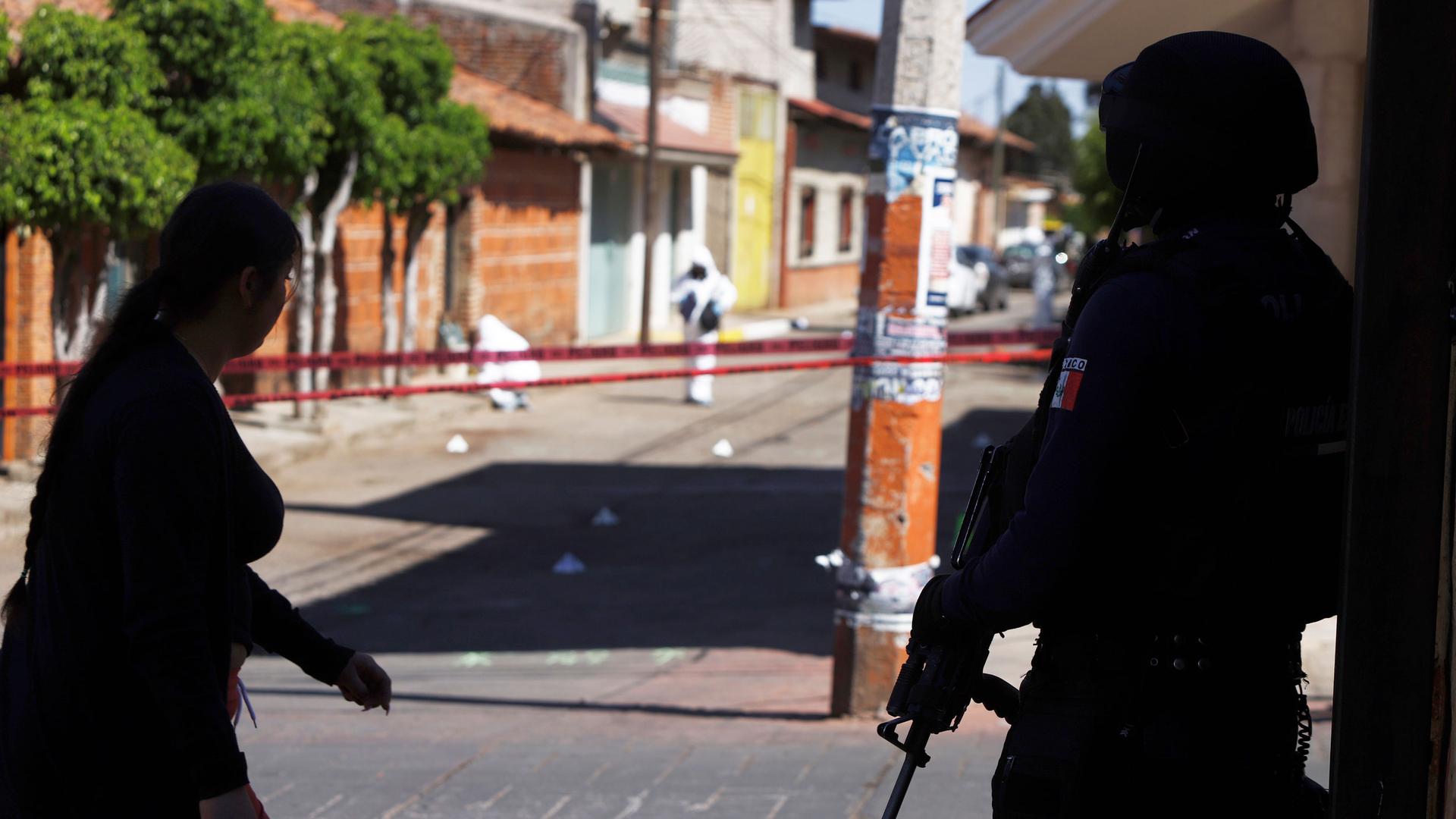 A police officer guards the area as investigators comb the site where more than a dozen people were believed to have been gunned down by armed men on Sunday, in San Jose de Gracia, head of the municipality of Marcos Castellanos, in Michoacan state, Mexico
