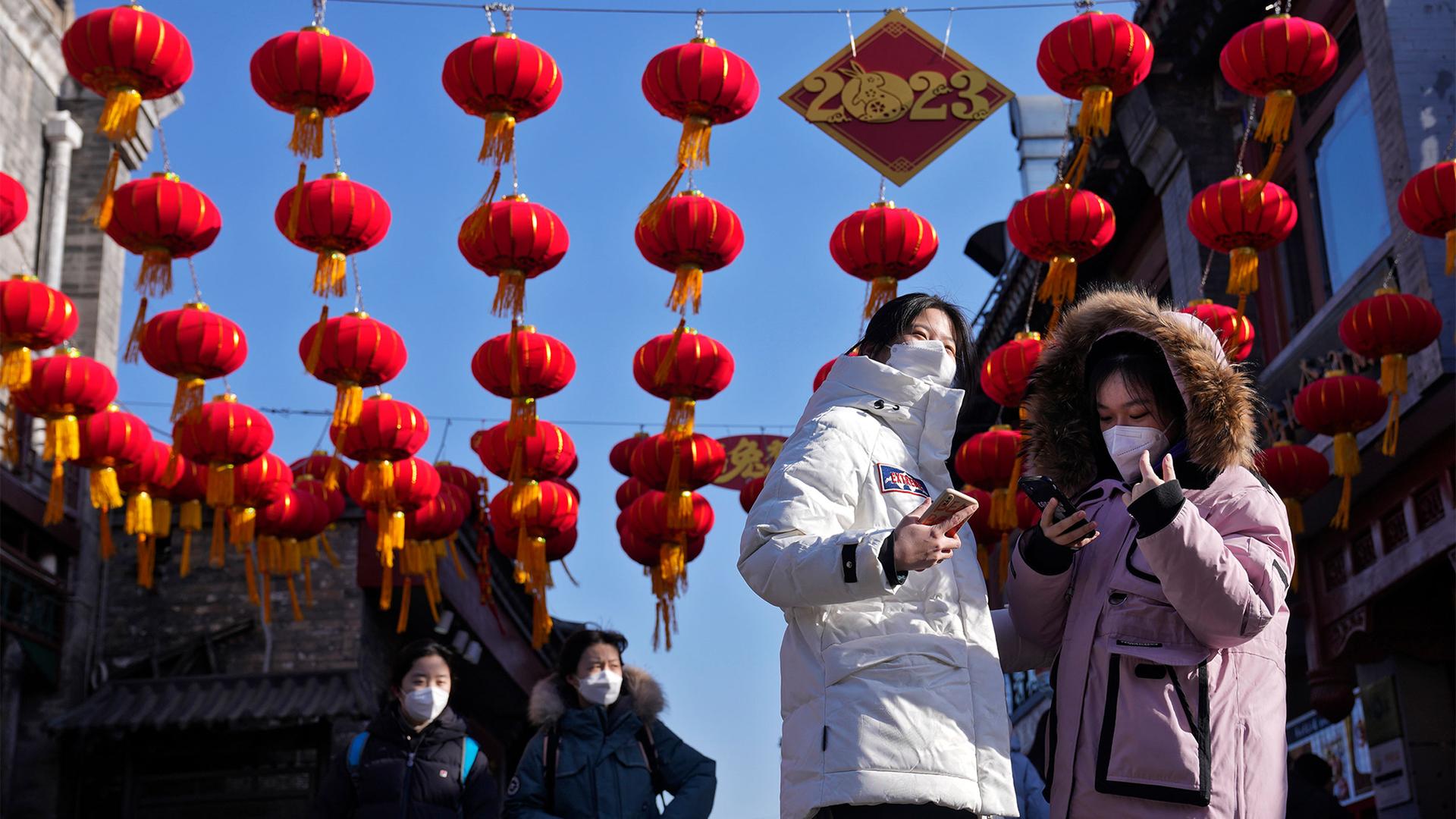 Women wearing face masks take souvenir photos as visitors tour past red lanterns hanging on a shopping alley near the Houhai Lake for celebrating the Lunar New Year in Beijing, Jan. 16, 2023.