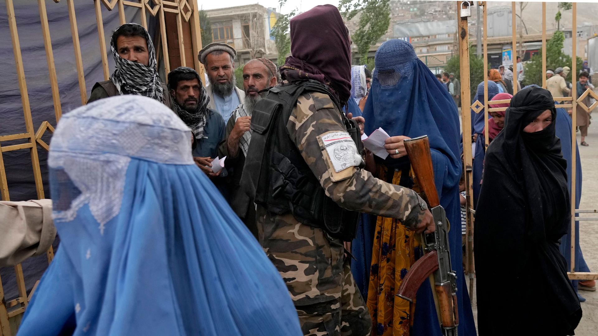 A Taliban fighter stands guard as people wait to receive food rations distributed by a South Korean humanitarian aid group, in Kabul, Afghanistan, May 10, 2022.