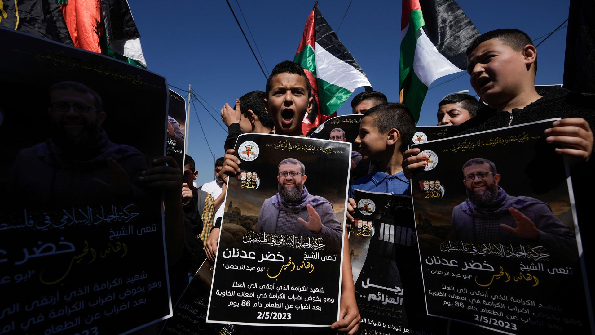 Palestinian kids wave their national flag and hold posters showing Khader Adnan, a Palestinian Islamic Jihad militant who died in Israeli prison after a nearly three-month hunger strike.