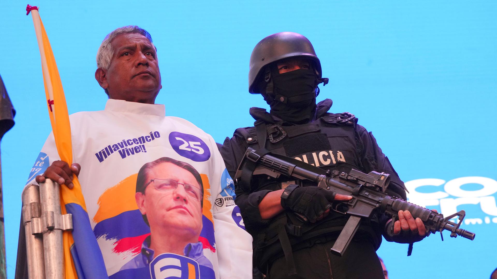 A supporter of the "Movement Construye" party wearing a shirt with the image of slain candidate Fernando Villavicencio, stands next to a police officer in tactical gear during a Catholic Mass prior to their closing campaign rally in Quito, Ecuador, Thursd