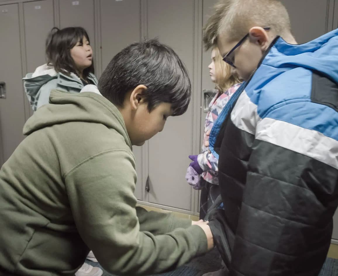 Artem's friend stops to help him zip up his jacket before recess.