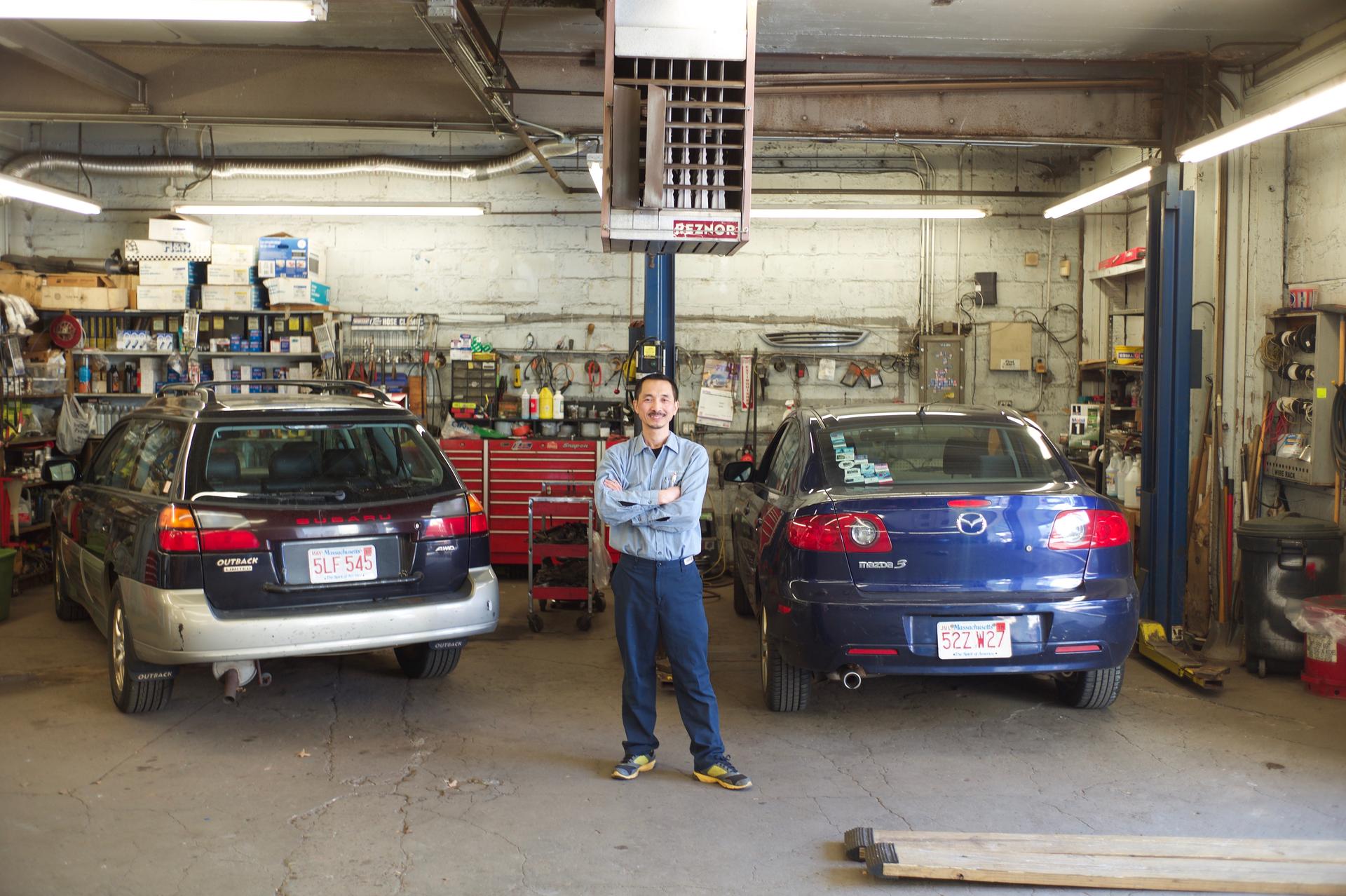 Guang Lin stands with cars in his Cambridge shop.