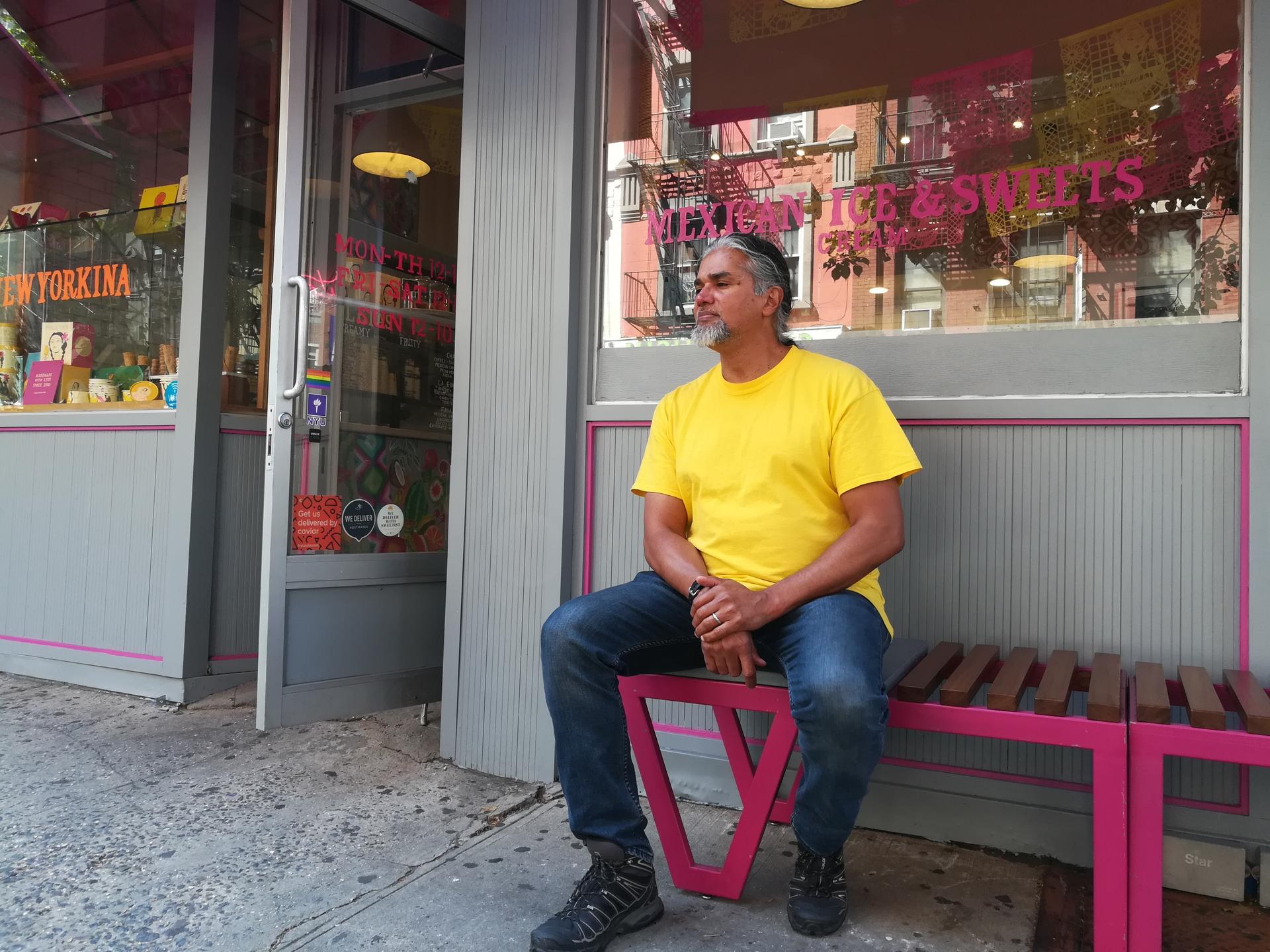 Man sitting on bench in front of sweets shop, looking off camera
