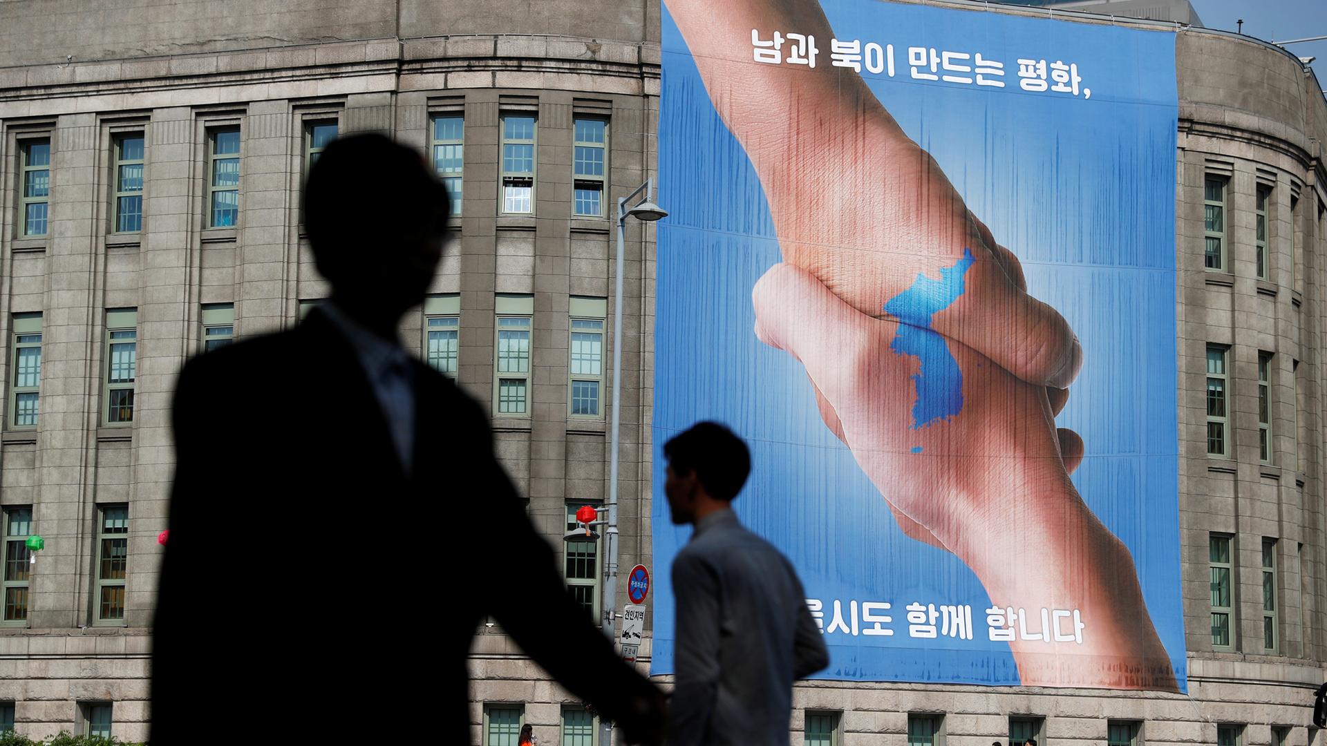 People walk past a large banner adorning the exterior of City Hall ahead of the upcoming summit between North and South Korea in Seoul.