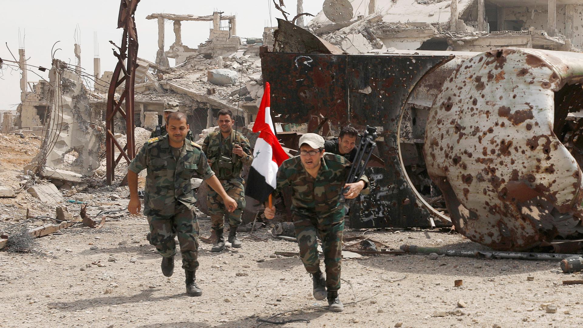Soldiers loyal to Syria's President Bashar al-Assad are seen running toward the camera with one carrying the Sryian flag.