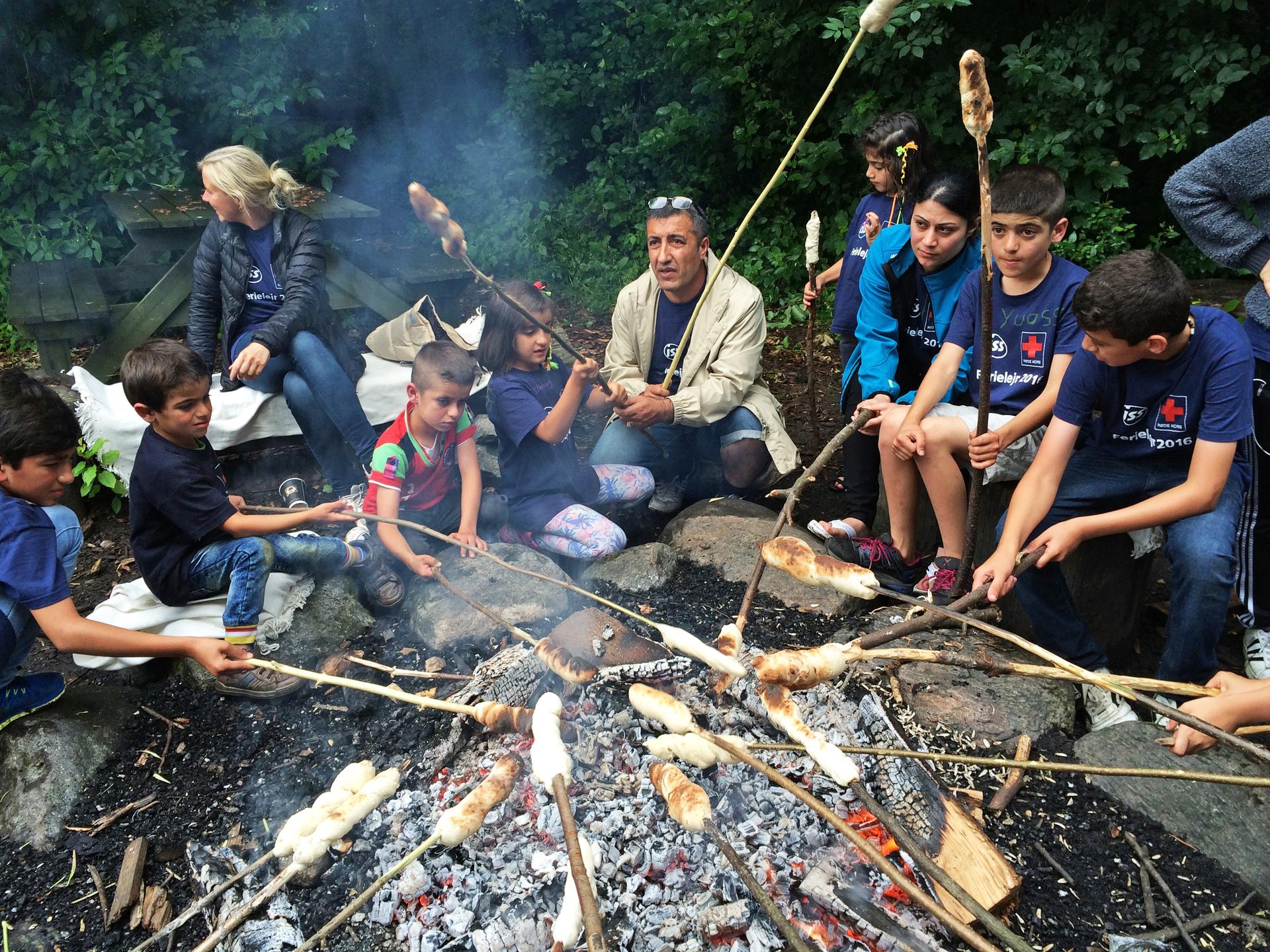 Mohamad Sheikh Ali and his daughter (center) bake bread at a campfire in Denmark. They fled dangers in Syria before it was too late.