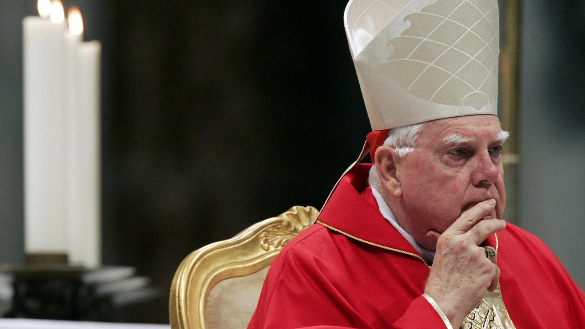 Cardinal Bernard Law, with a hand to his mouth, looks off.