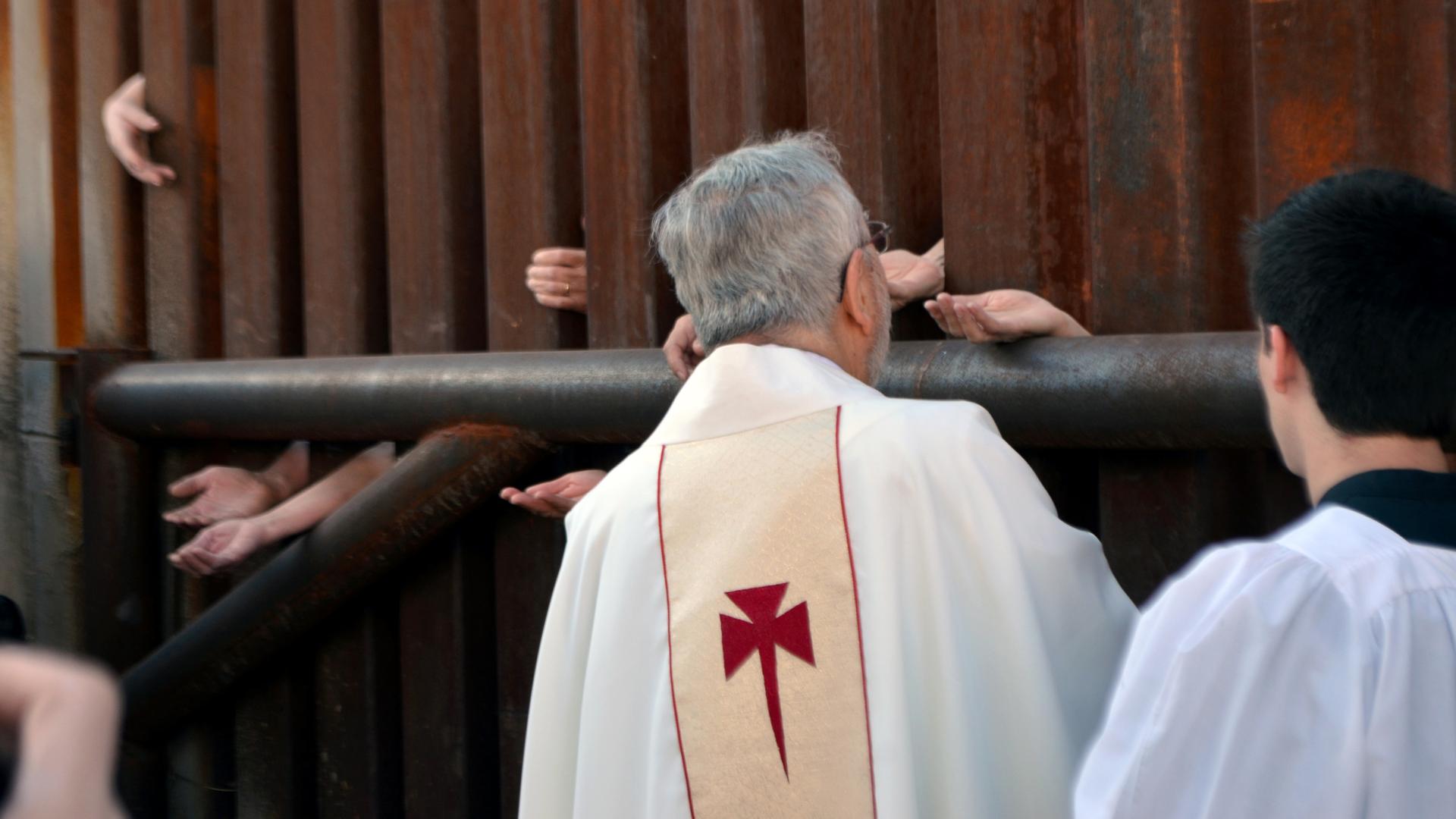 People on the Mexican side of the border reach through fence in Nogales, Arizona, to receive Holy Communion from the Bishop of Tucson, Gerald Kicanas.