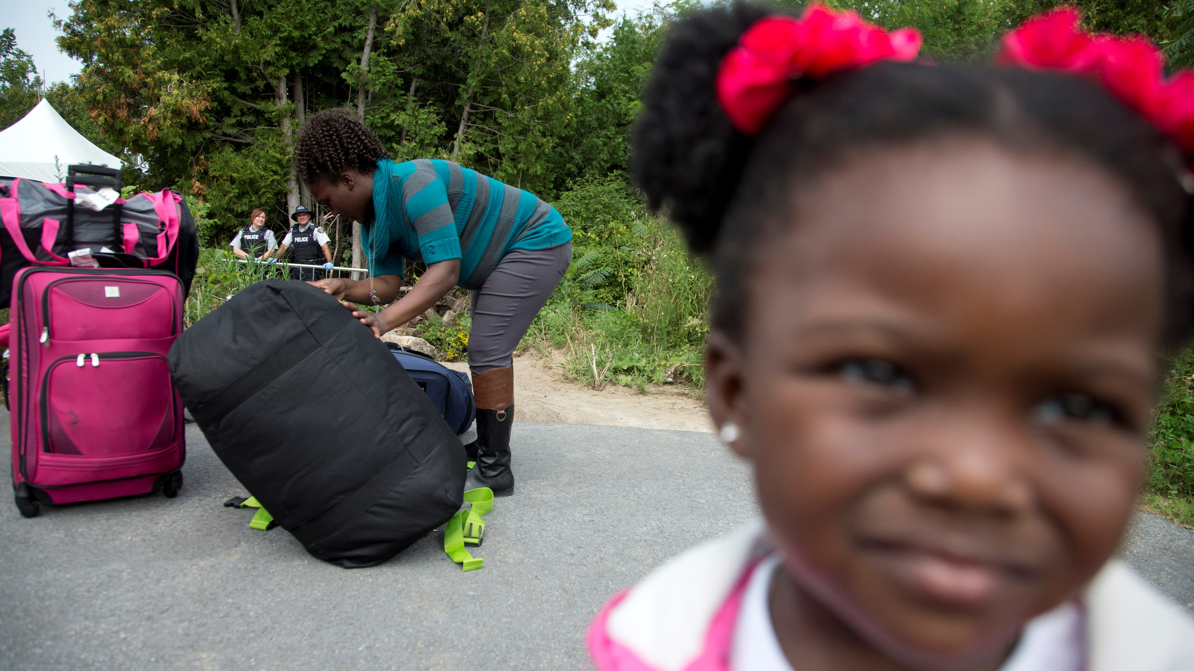 A mother and her young daughter are watched by Royal Canadian Mounted Police (RCMP) officers as they prepare to cross the US-Canada border from New York into Quebec earlier this month. Like thousands of others fleeing the US for Canada, the woman told off