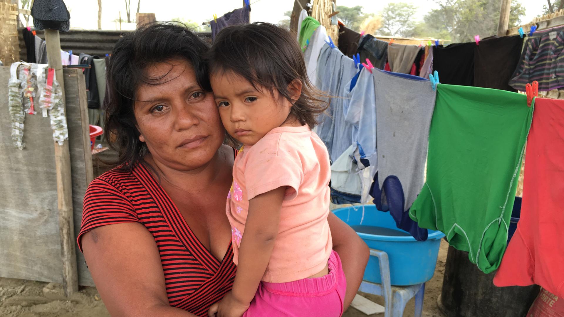 Flor Bautista holds her daughter Camila in her arms, both looking directly at camera.