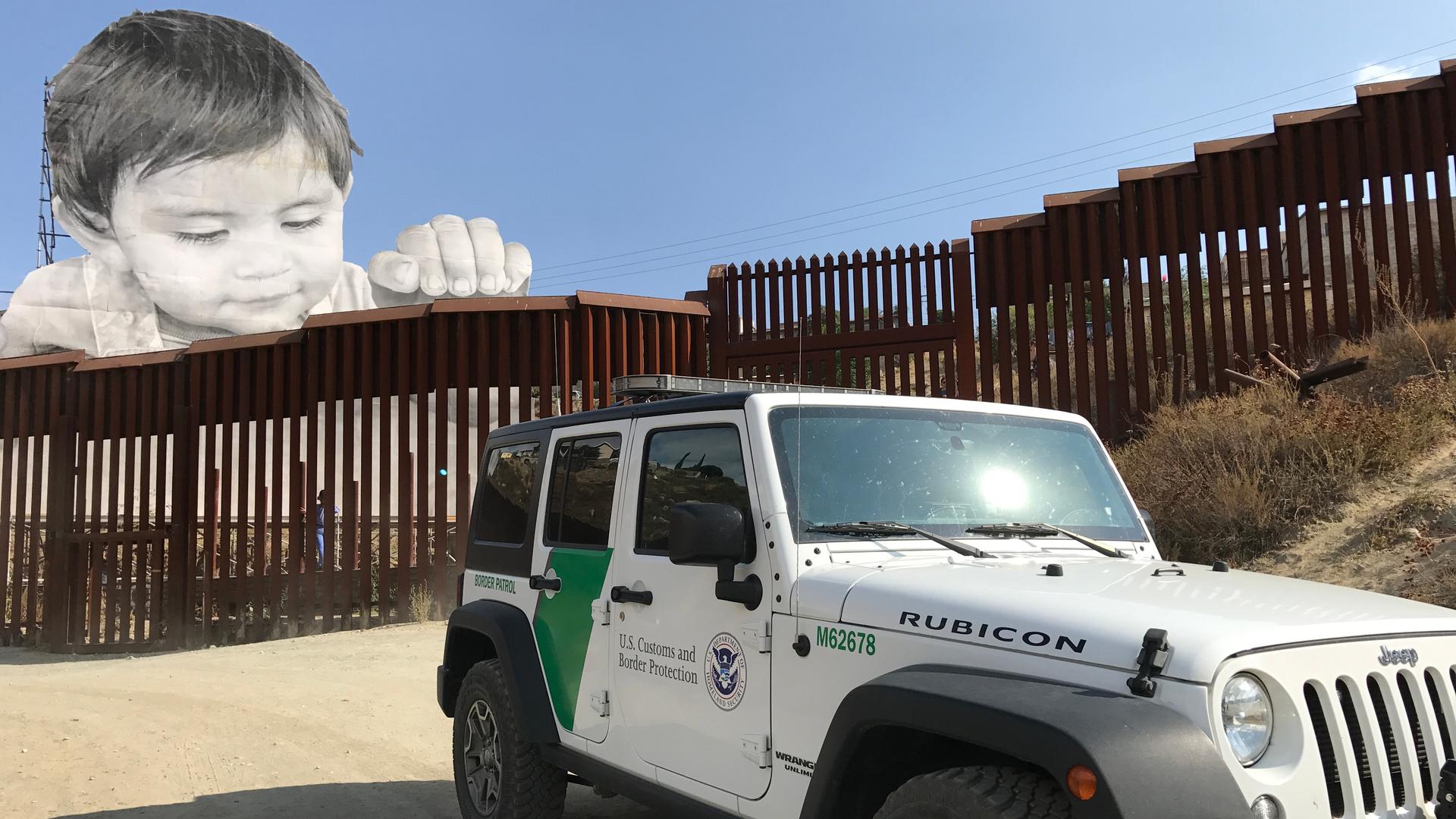 Large photo installed on one side of metal fencing looks out over Border Patrol SUV