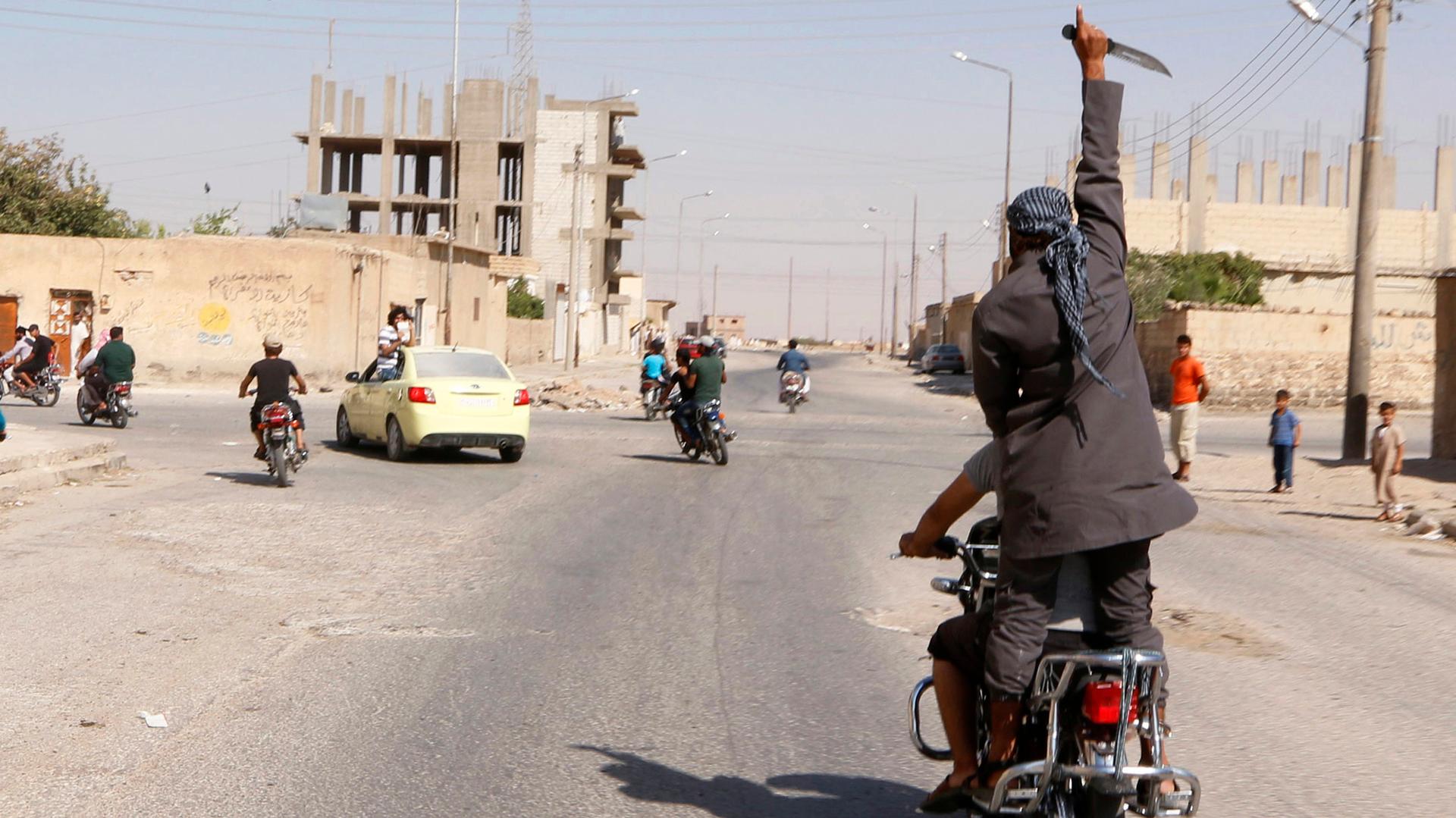 A man holds up a knife as he rides on the back of a motorcycle touring the streets of Tabqa in celebration after ISIS militants took over Tabqa air base in Syria, on August 24, 2014.