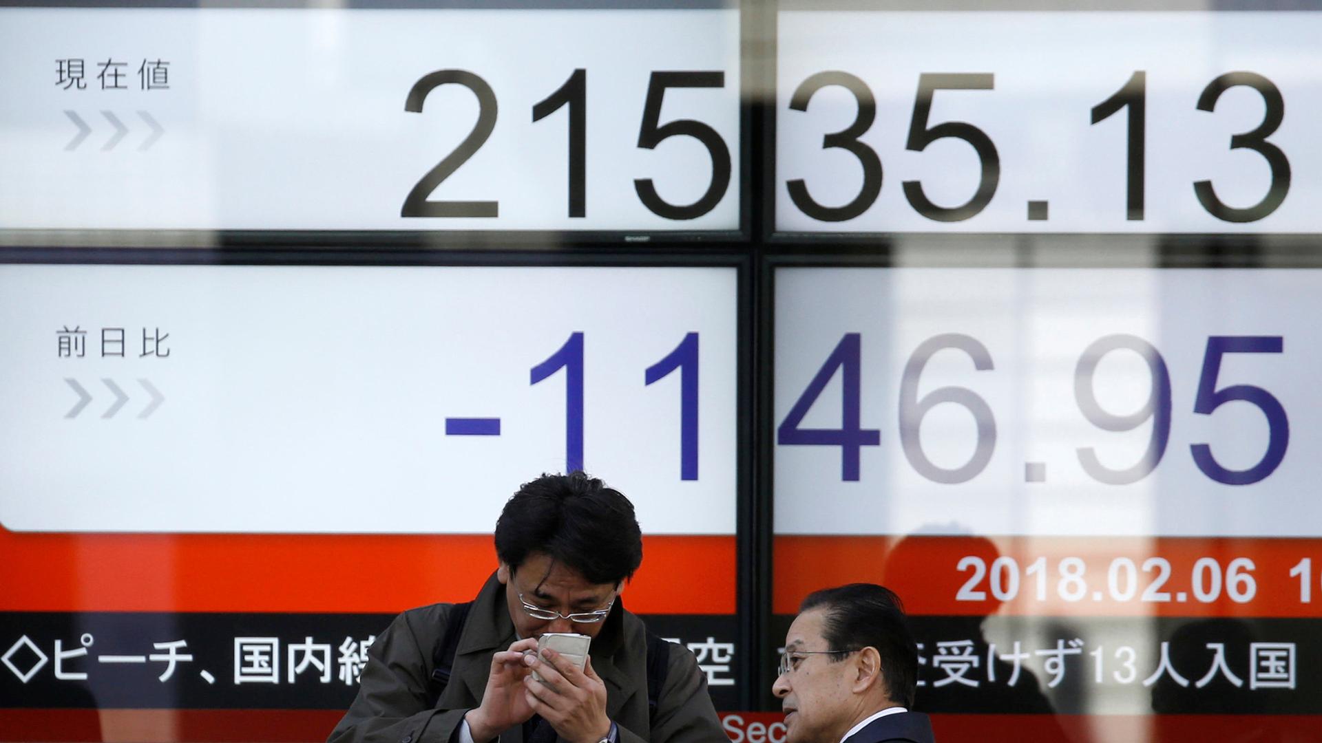 A man looks at a mobile phone in front of an electronic board showing Japan's Nikkei average outside a brokerage in Tokyo, Japan.