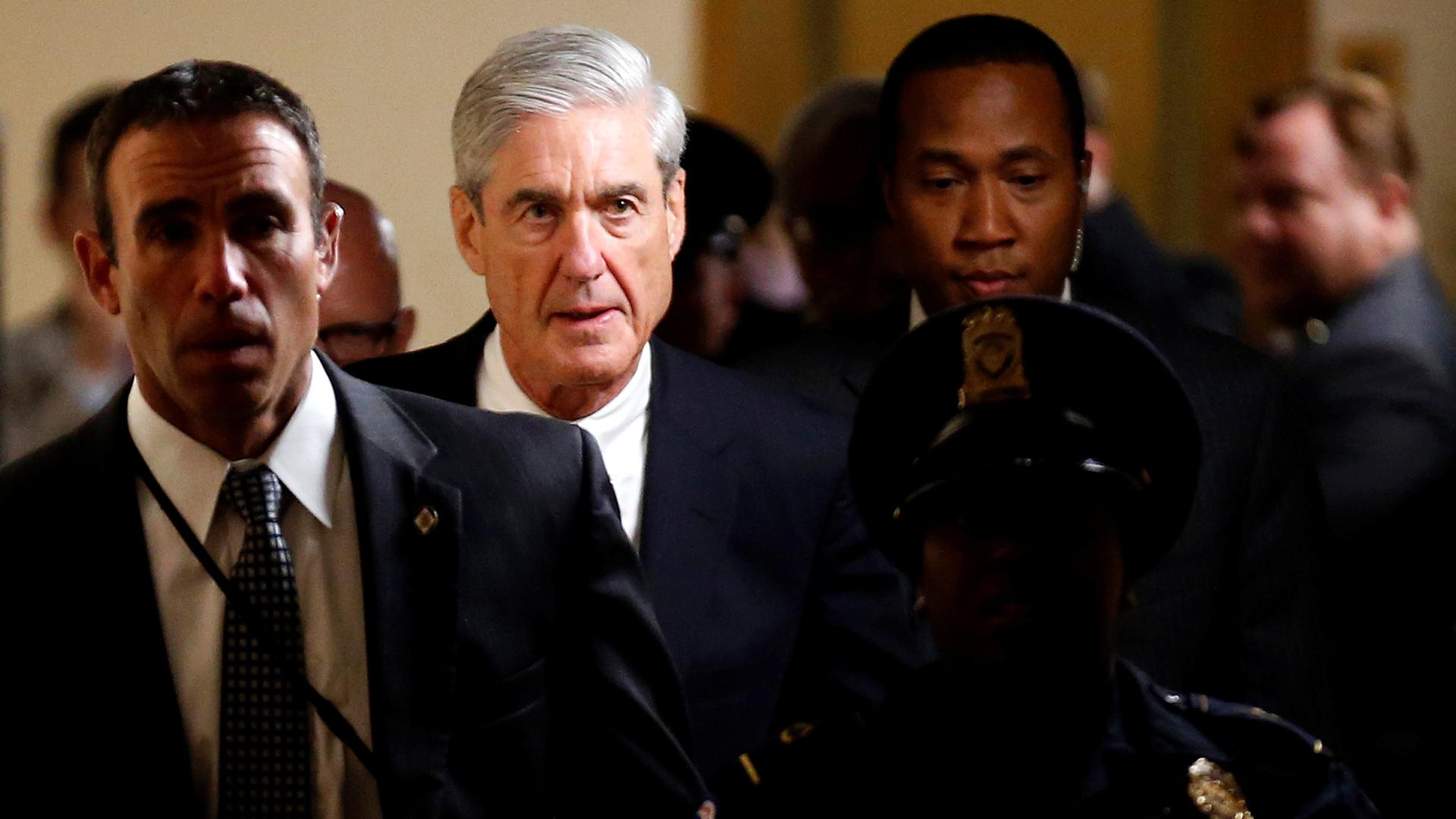 Special Counsel Robert Mueller is shown walking down a hallway surrounded by staff and police.