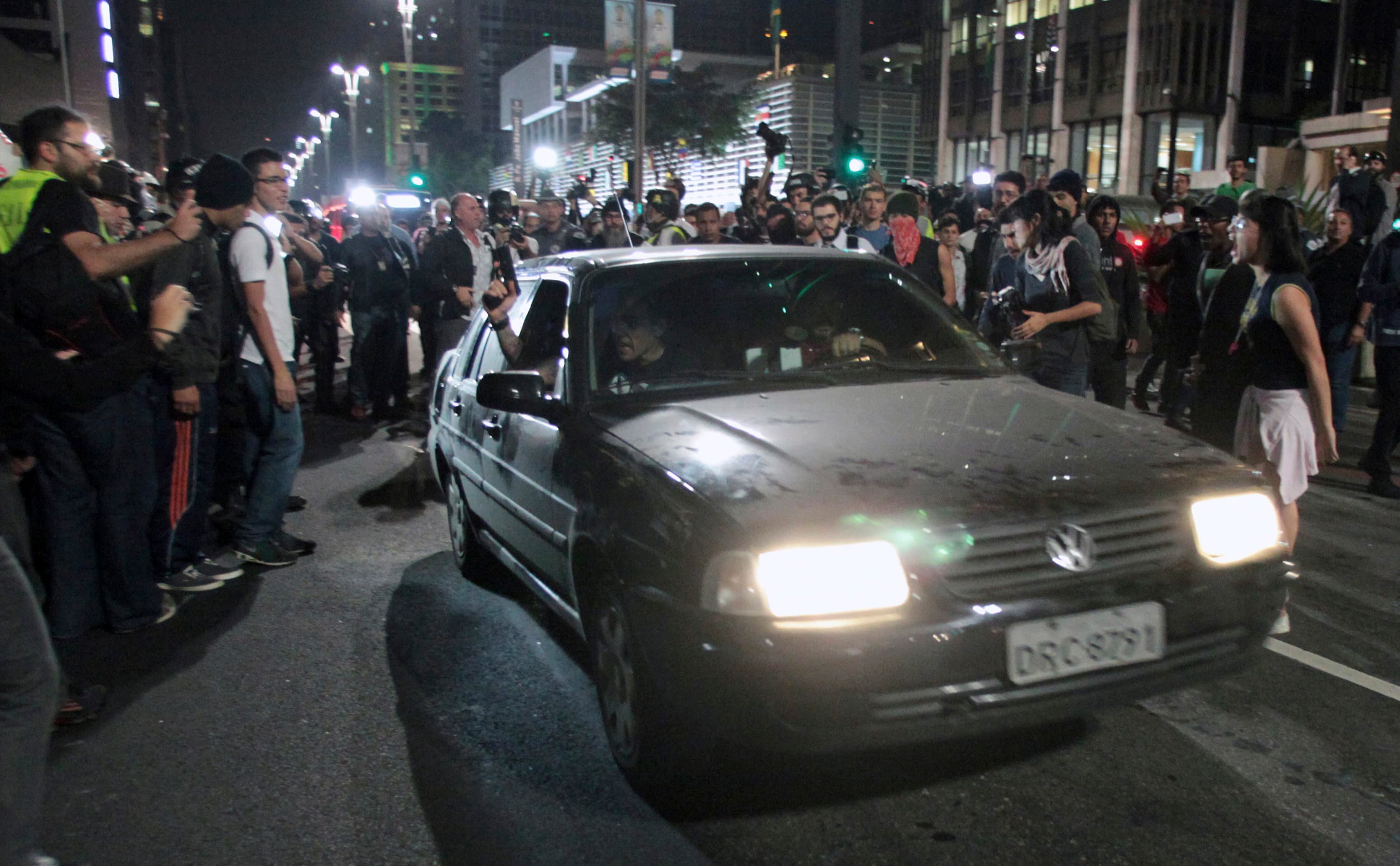 A Brazilian policeman pulls a gun out of the window of a car during a June 23 protest against the World Cup on a street in São Paulo. Activists say the arrests of two men at those protests were trumped up by police.