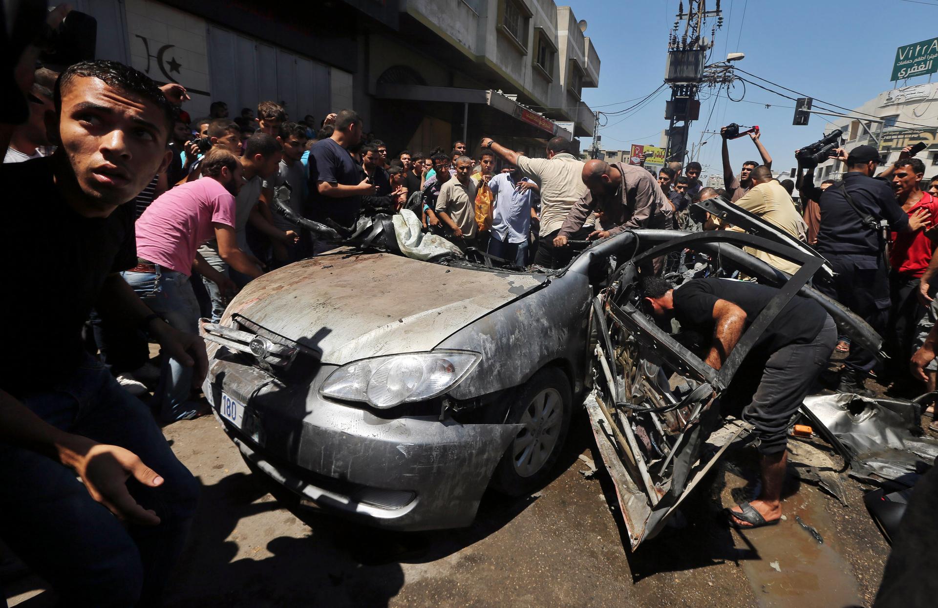 Palestinians in Gaza City gather around the remains of a car which police said was targeted in an Israeli air strike on Tuesday.