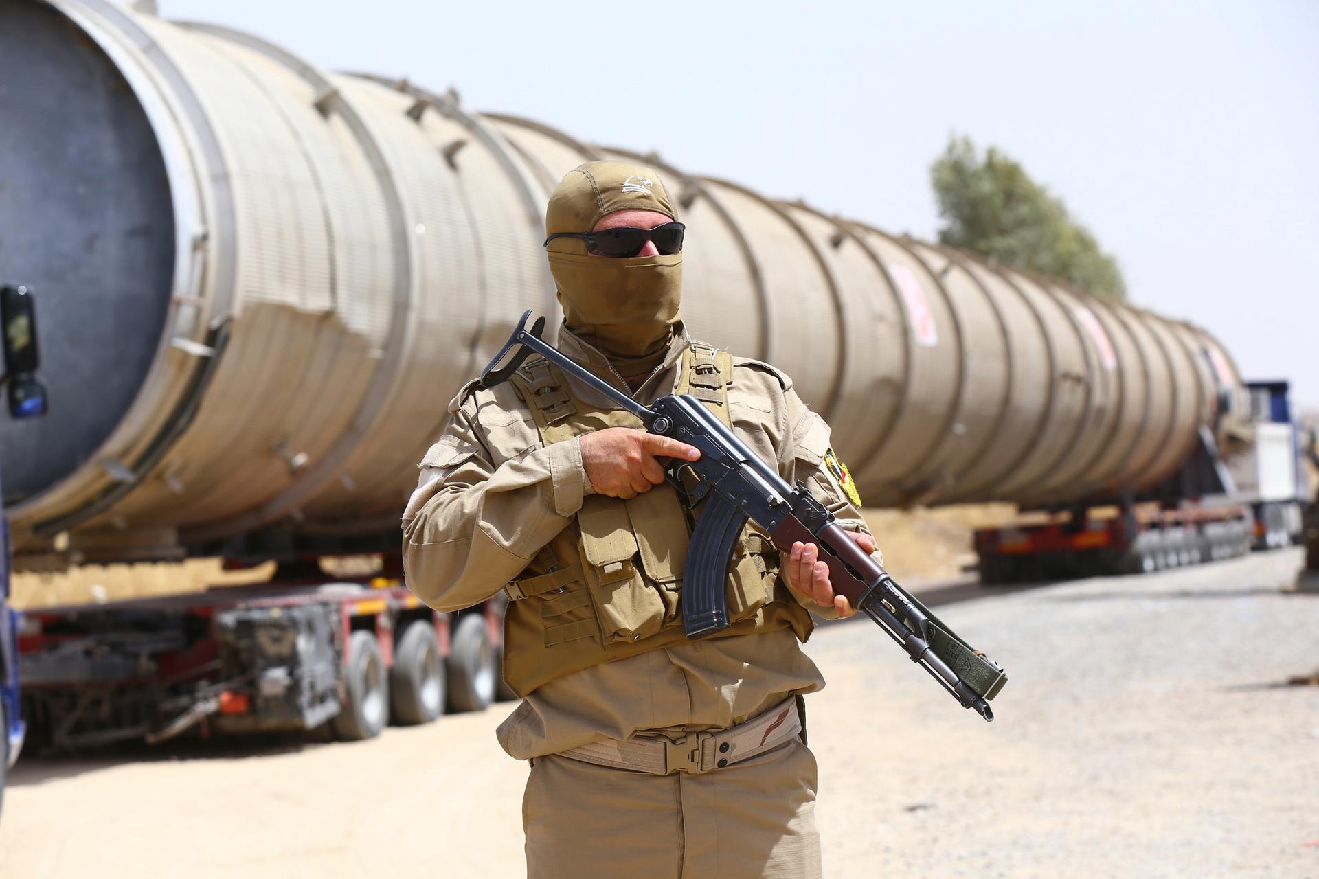 A member of the Kurdish security forces takes up position with his weapon as he guards a section of an oil refinery.