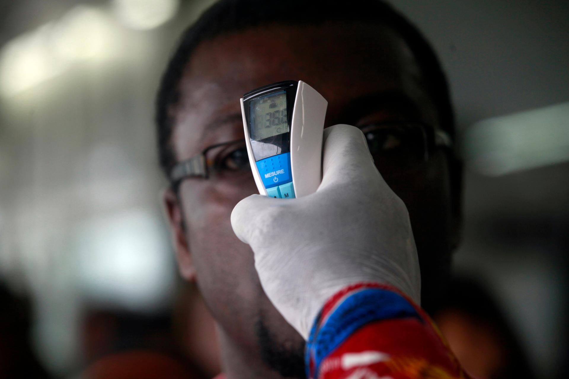 A health worker takes a passenger's temperature with an infrared digital laser thermometer at the Felix Houphouet Boigny international airport in Abidjan on August 13, 2014.