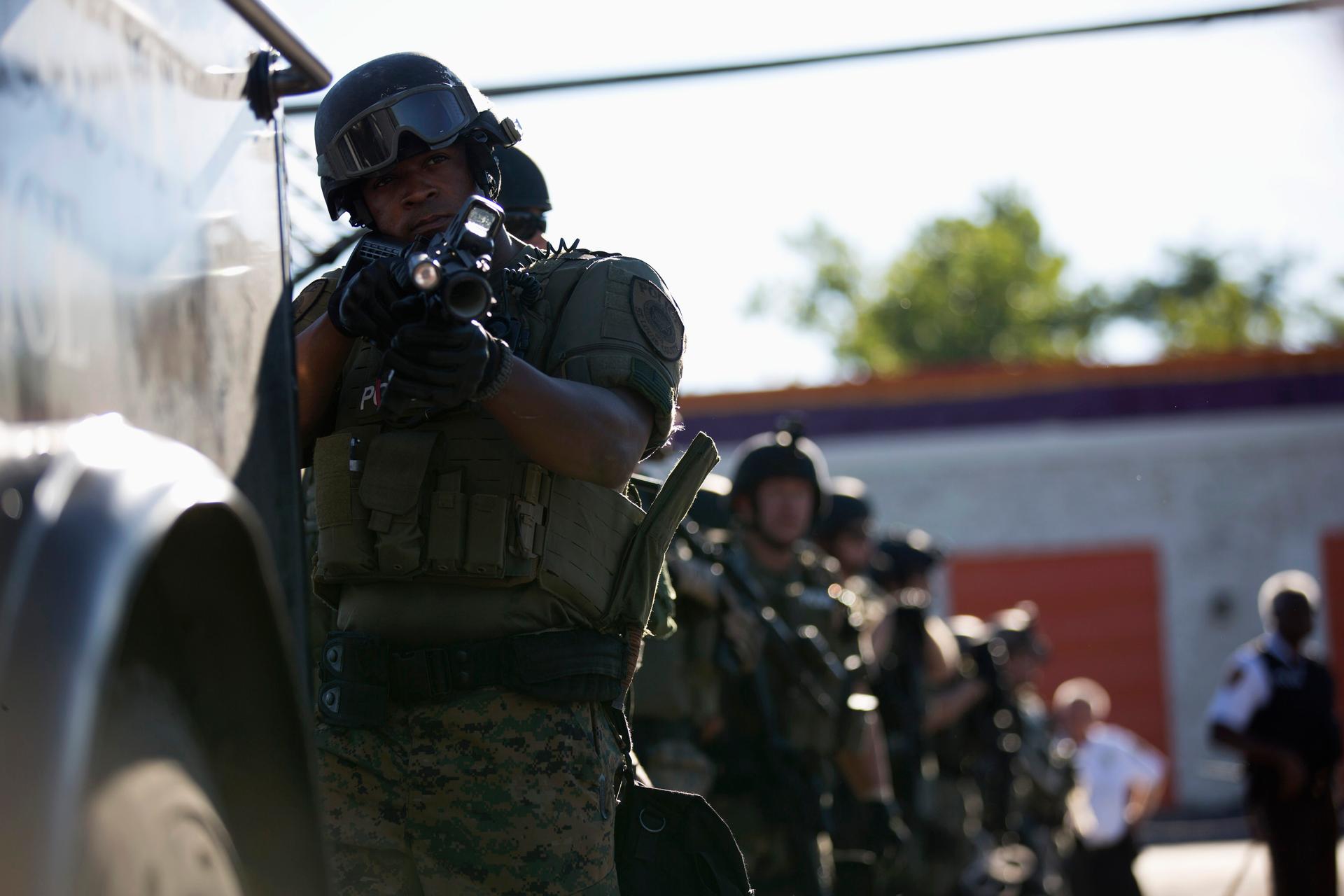 A police officer holds his riot gun while demonstrators protest the shooting death of teenager Michael Brown in Ferguson, Missouri, on August 13, 2014.