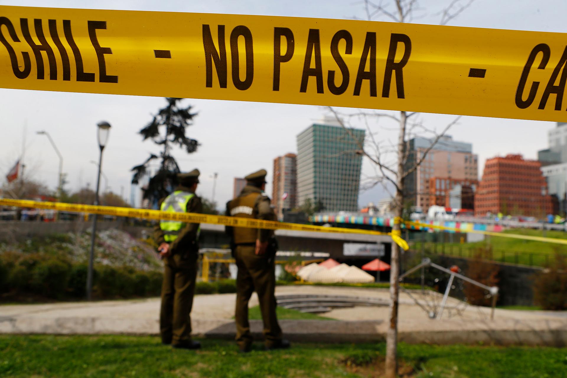 Police officers are seen behind barricade tape guarding an area where a bomb exploded in Santiago September 8, 2014. The words on the yellow tape read, "Do not pass."