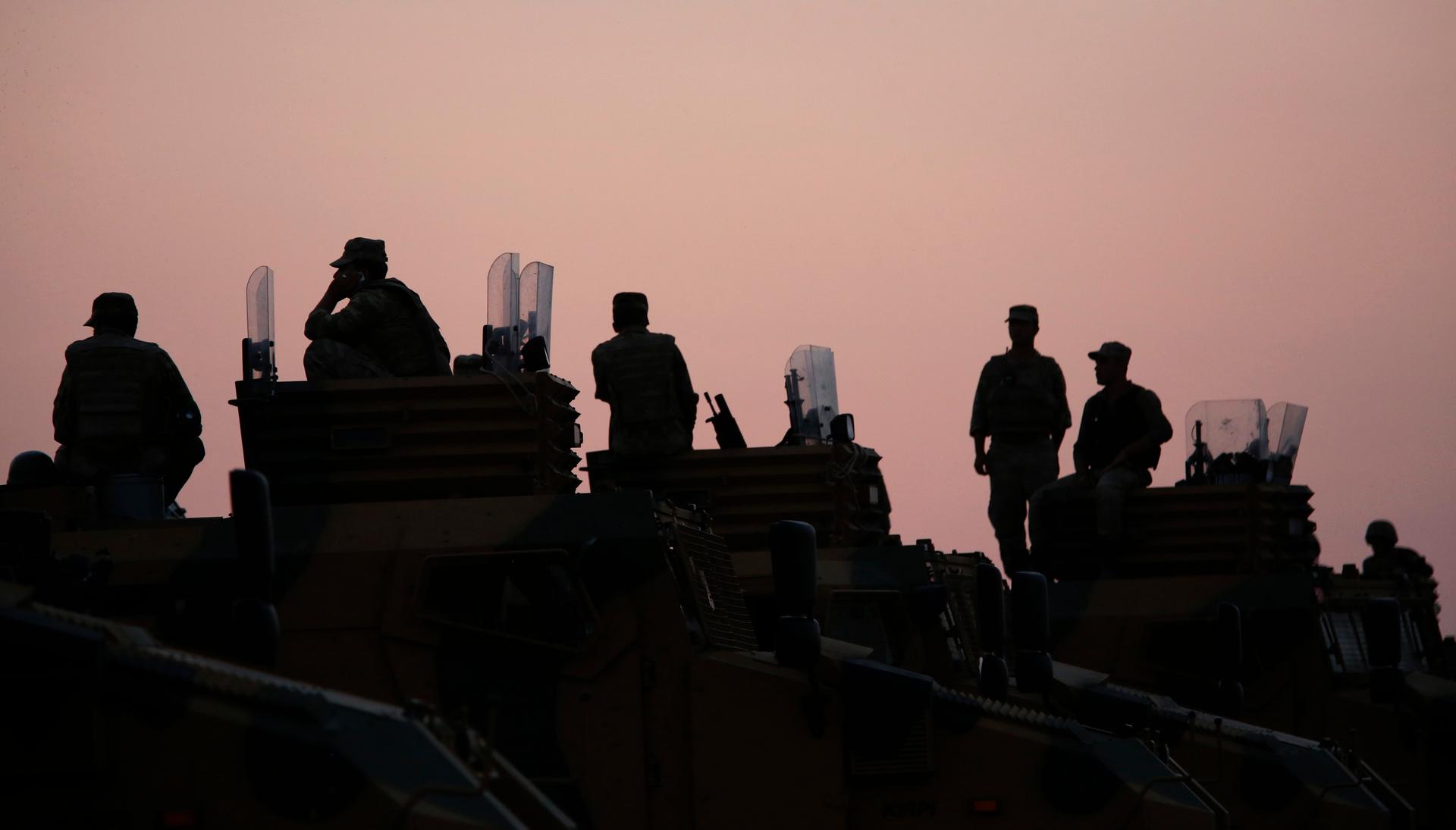 Turkish soldiers are silhouetted atop armoured vehicles near the Mursitpinar border crossing on the Turkish-Syrian border on October 3, 2014.
