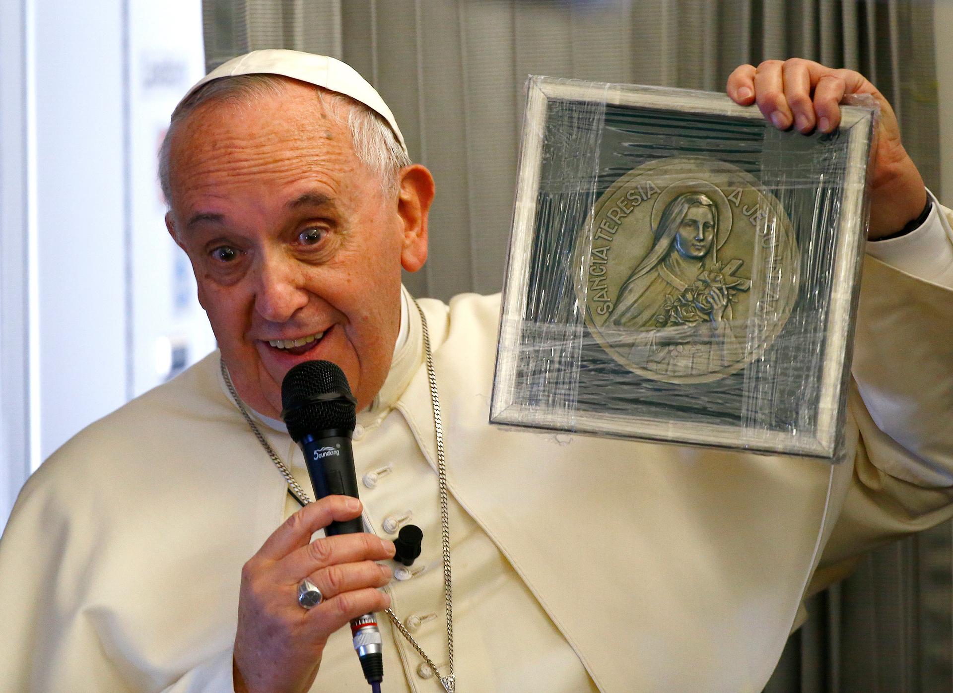Pope Francis holds up a plaque with an image of Saint Theresa during a meeting with journalists on his flight from Colombo, Sri Lanka, to Manila in the Philippines on January 15, 2014.