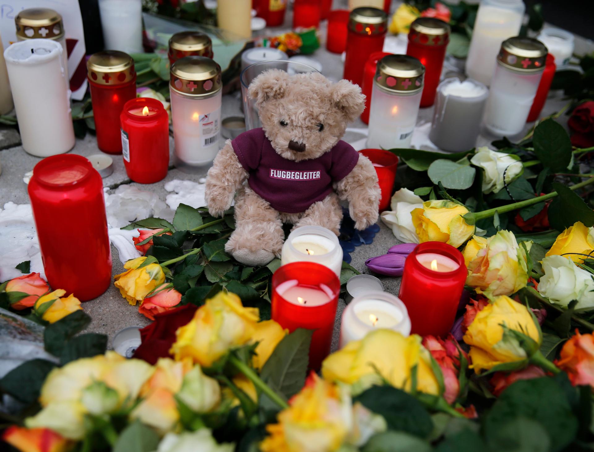 A teddy bear wearing a shirt with the word "flight attendant" is placed between flowers and candles outside Germanwings headquarters at the Cologne Bonn airport on March 25, 2015.
