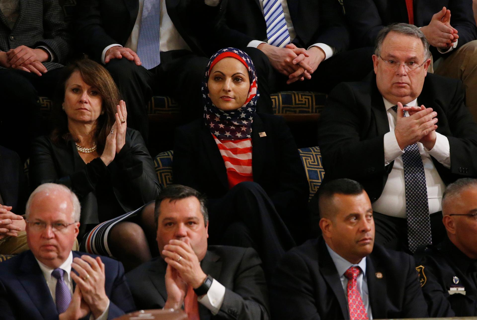 Woman in hijab with American flag pattern amongst men in suits and one woman in black shirt