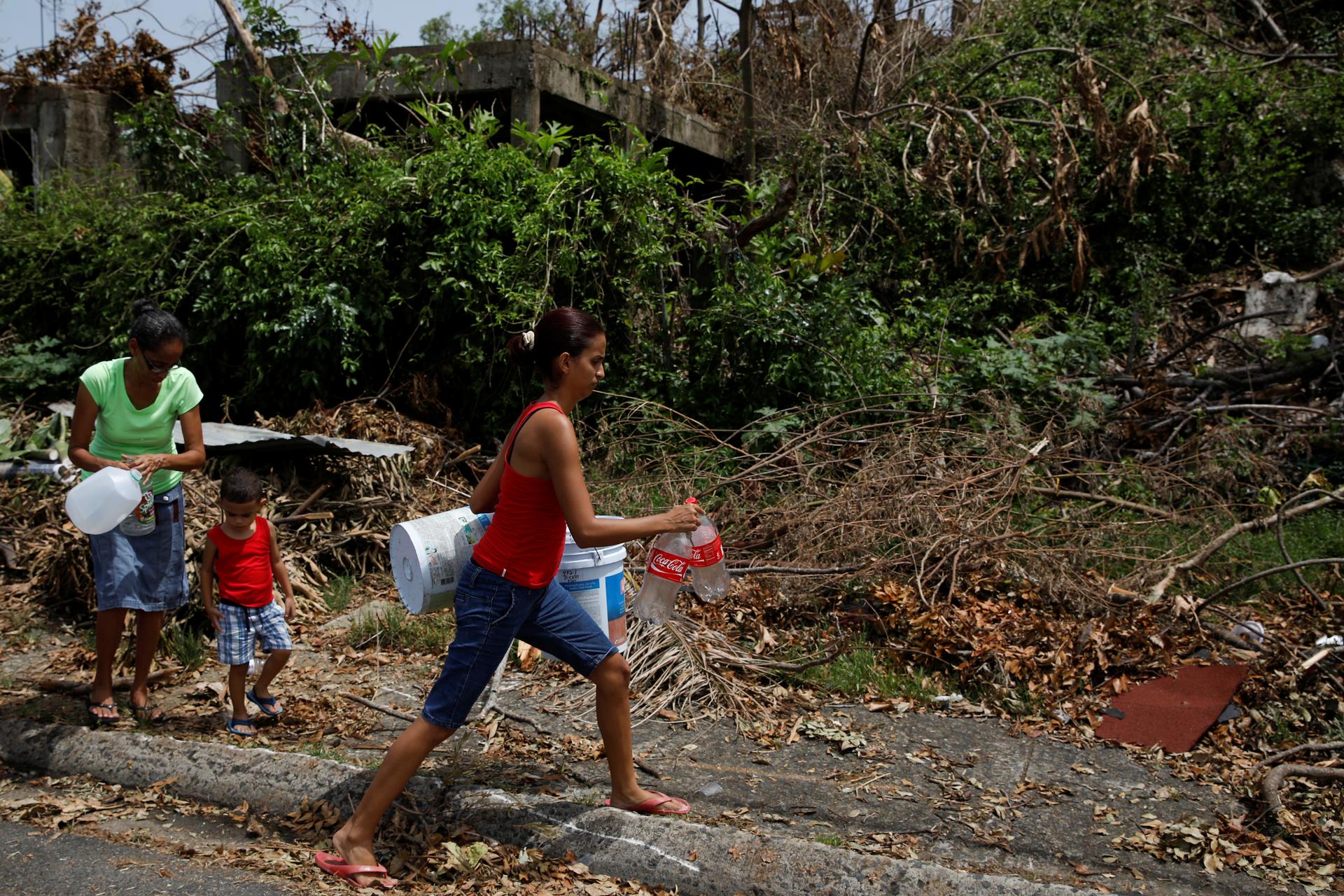 People carry containers that will be filled with water from a tank truck at an area hit by Hurricane Maria in Canovanas, Puerto Rico, Sept. 26, 2017.