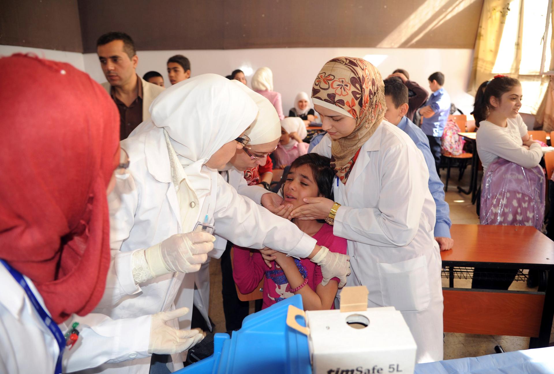 Syrian health workers administer polio vaccination to a girl at a school in Damascus, in this file photo taken by Syria's national news agency SANA in October.