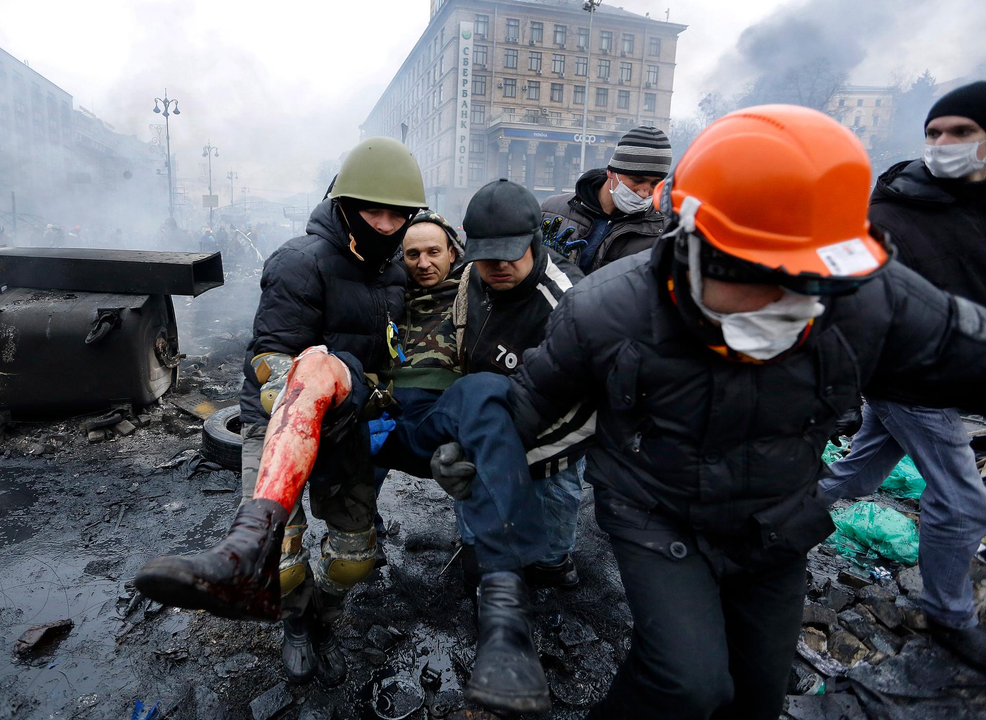 Anti-government protesters carry a man with a bullet wound on his leg during clashes with riot police in Independence Square in Kiev, February 20, 2014.