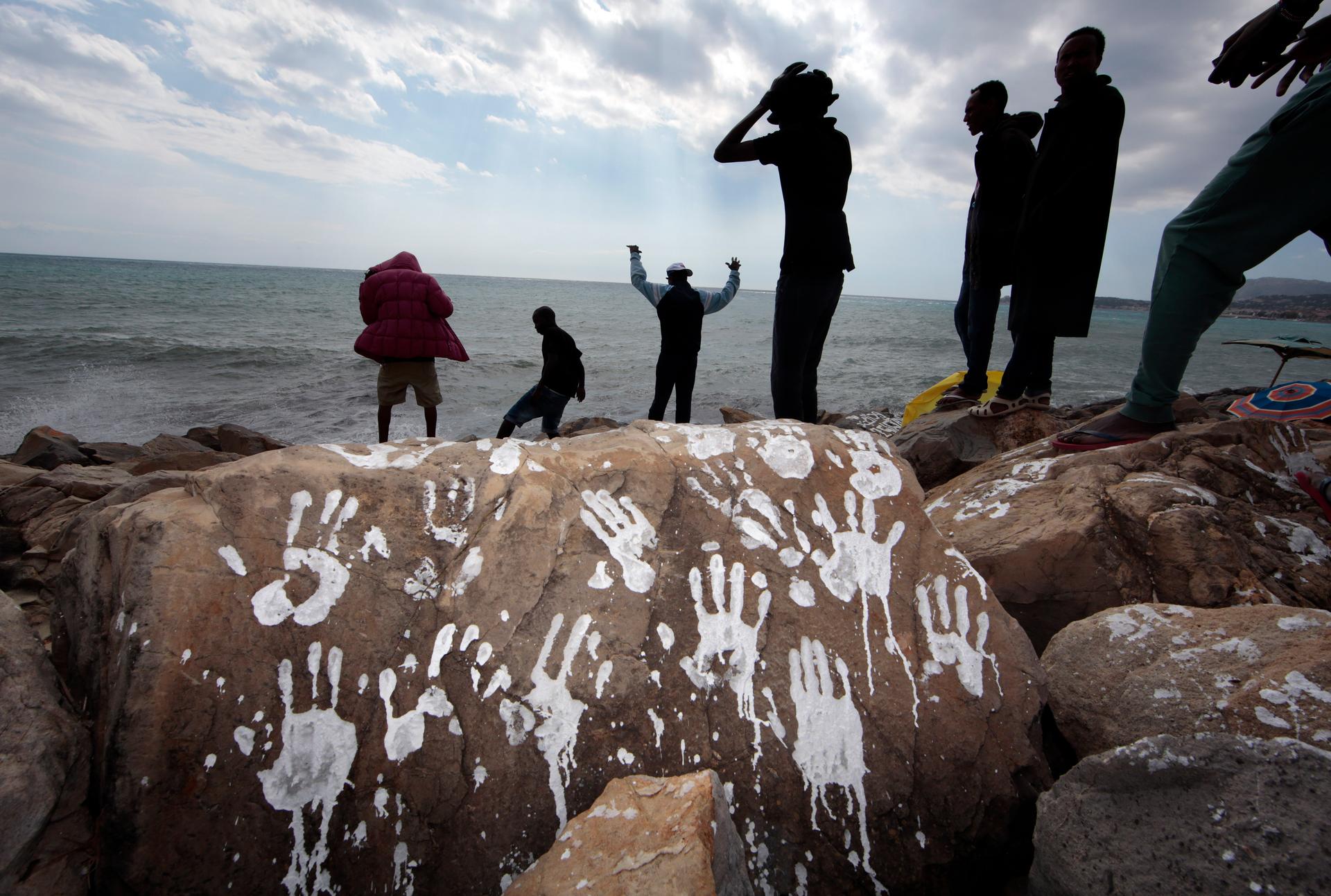 A group of Sudanese and Eritrean migrants are seen in silhouette near a rock with white hand prints on the seawall at the Saint Ludovic border crossing on the Mediterranean Sea between Vintimiglia, Italy and Menton, France, September 23, 2015.