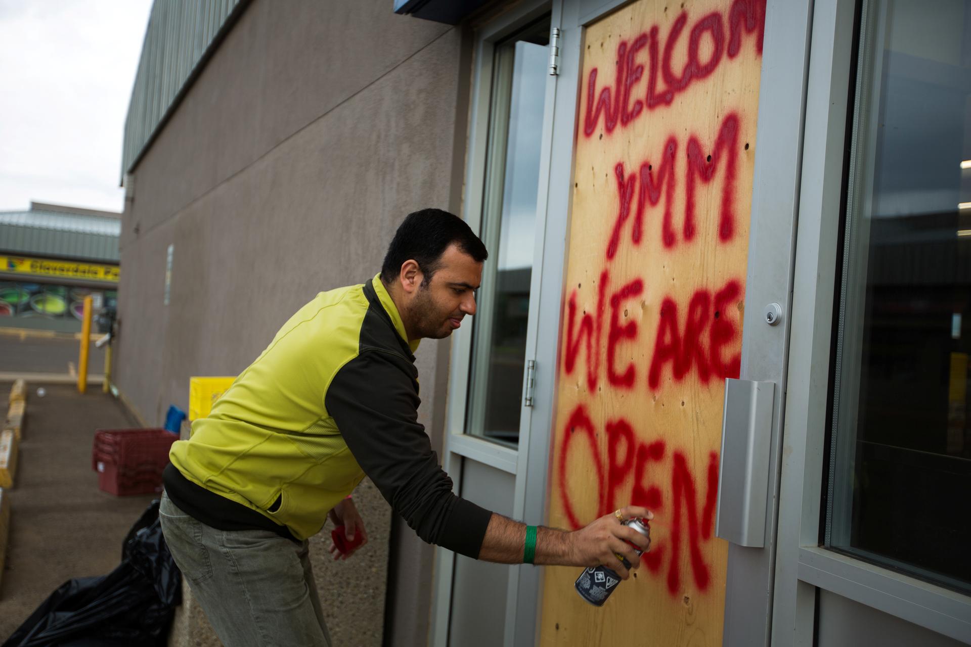 Convenience store manager Sunny Katoch paints a welcome sign on the back door as residents begin to flood back into their city after being evacuated due to raging wildfires in Fort McMurray, Alberta, Canada, June 1, 2016.