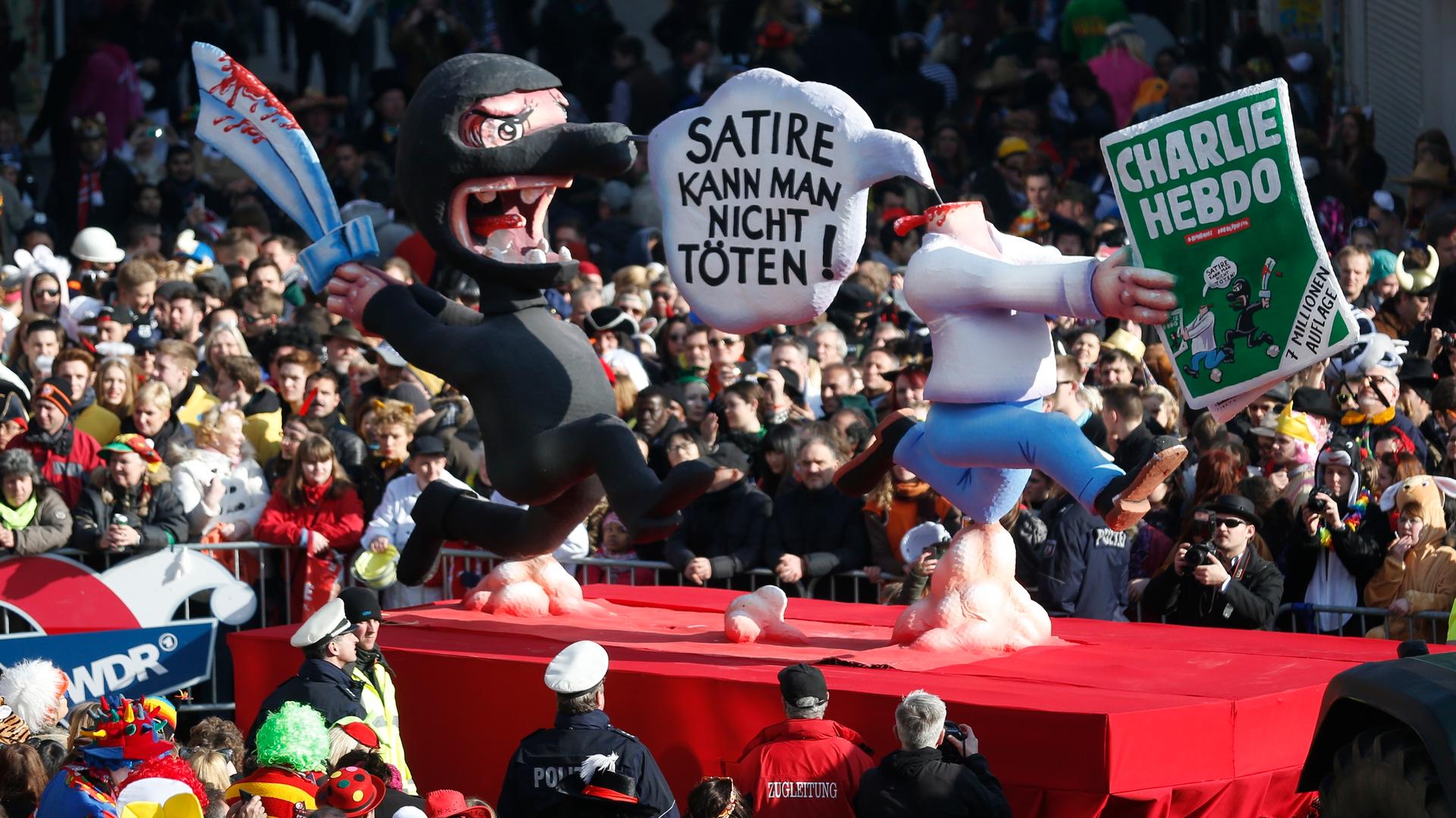 A carnival float by artist Jacques Tilly with a papier-mache caricature drives past revelers during the traditional 'Rose Monday' parade on Carnival in the western German city of Duesseldorf. "You can't kill satire," the sign reads.