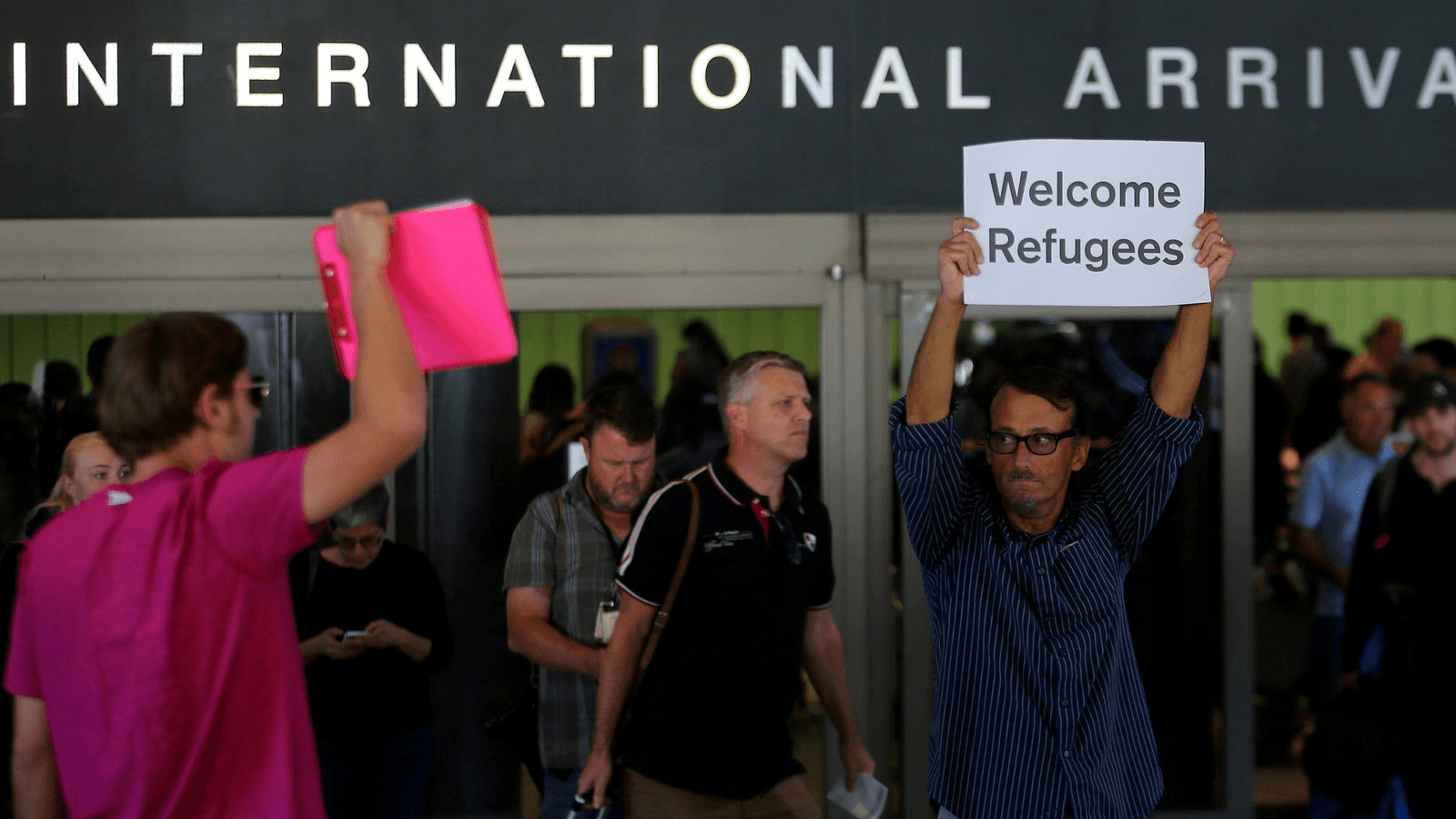 Retired engineer John Wider, 59, is greeted by a supporter of President Donald Trump as he holds up a sign reading "Welcome Refugees" at the international arrivals terminal at Los Angeles International Airport in Los Angeles, California, on June 29, 2017.