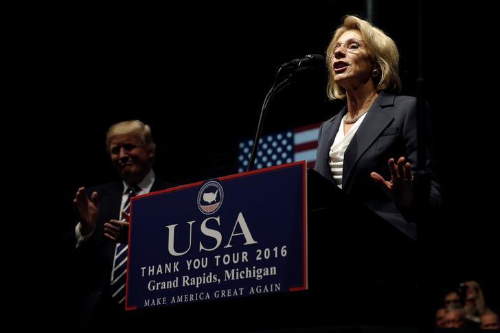 US President Donald Trump applauds Education Secretary nominee Betsy DeVos as she speaks at a podium.