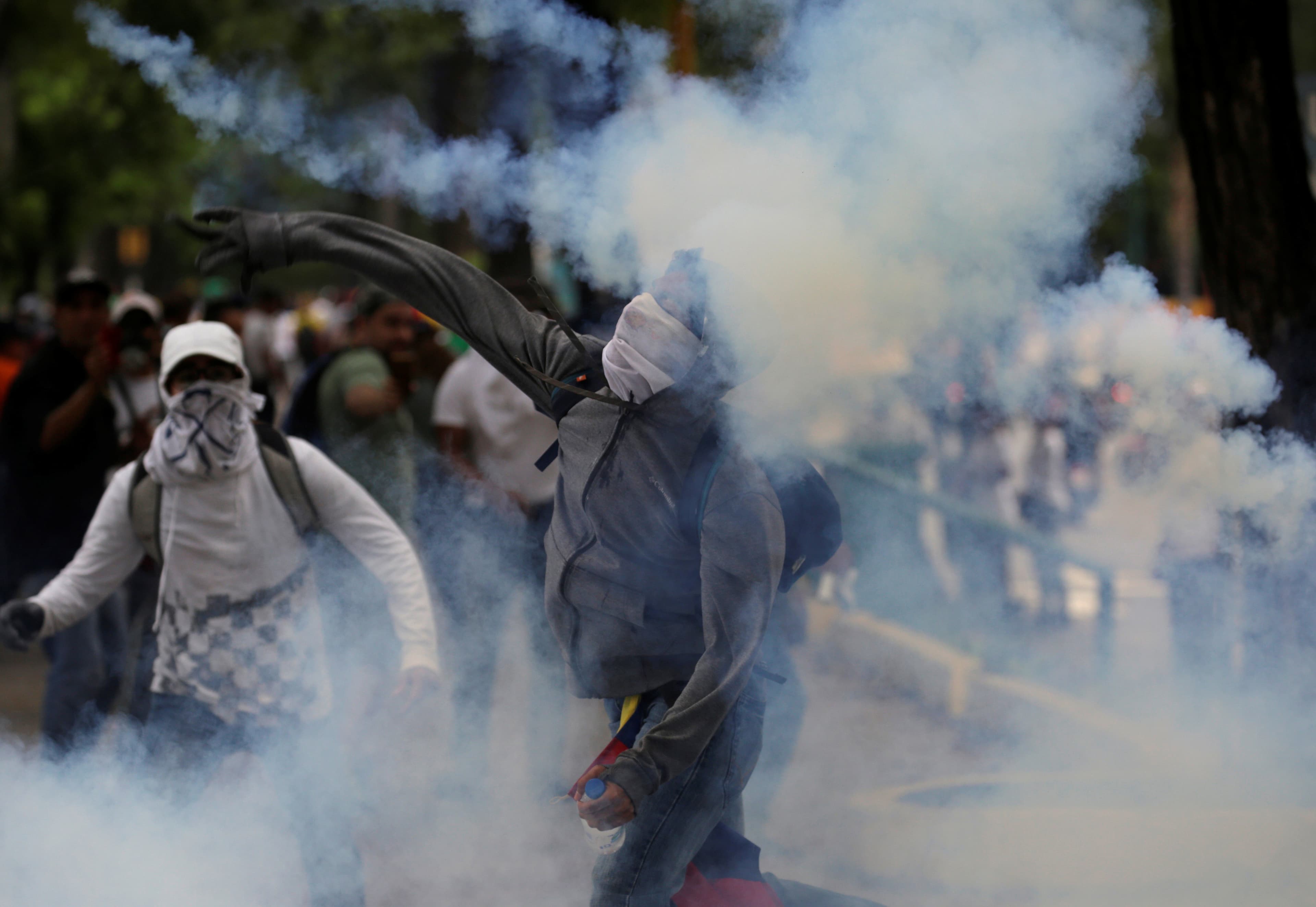 A demonstrator throws a tear gas canister back to police